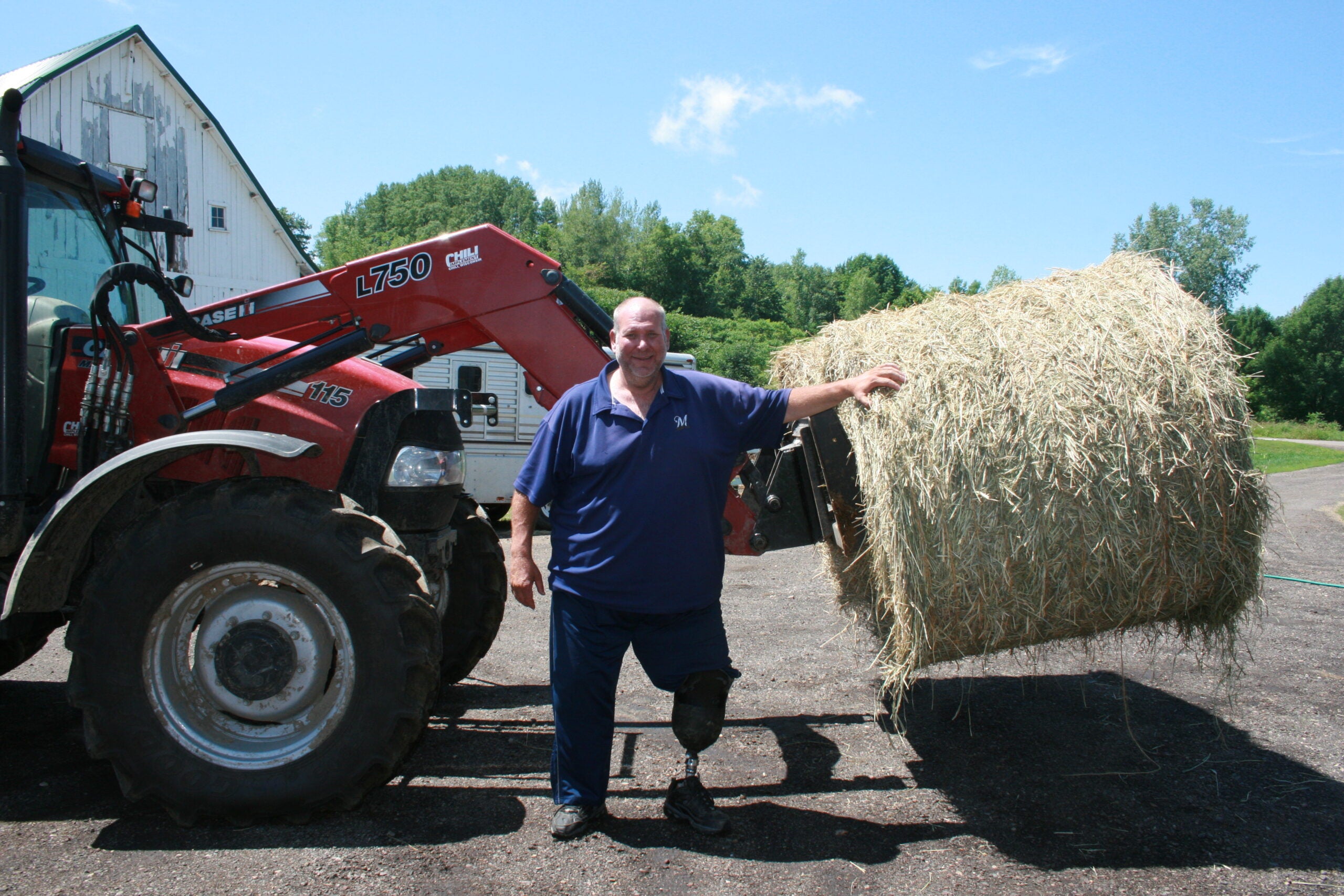 A farmer with a prosthetic leg poses in front of hay