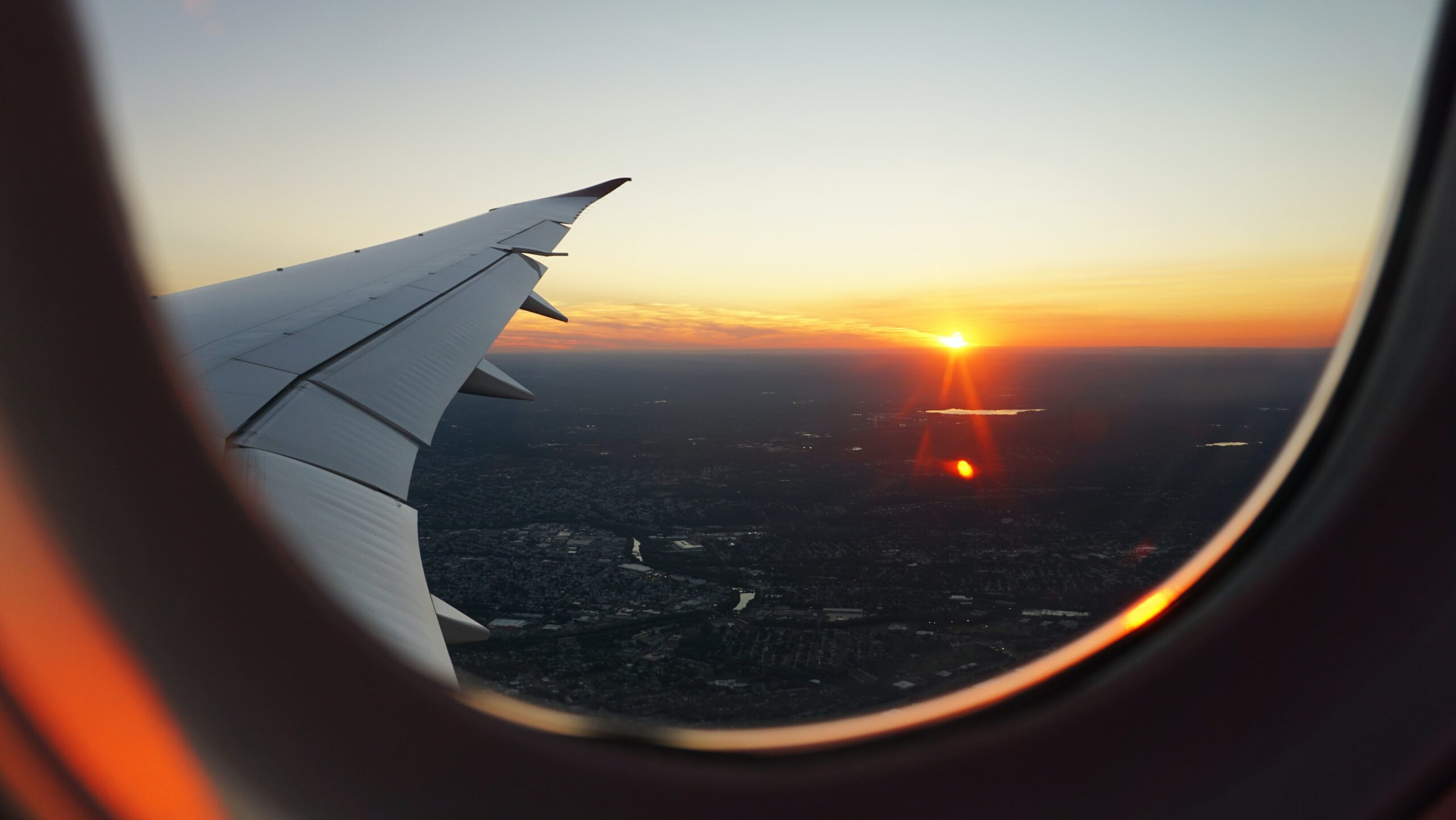 a sunset glows golden orange as viewed from the window of an airplane flying over a city