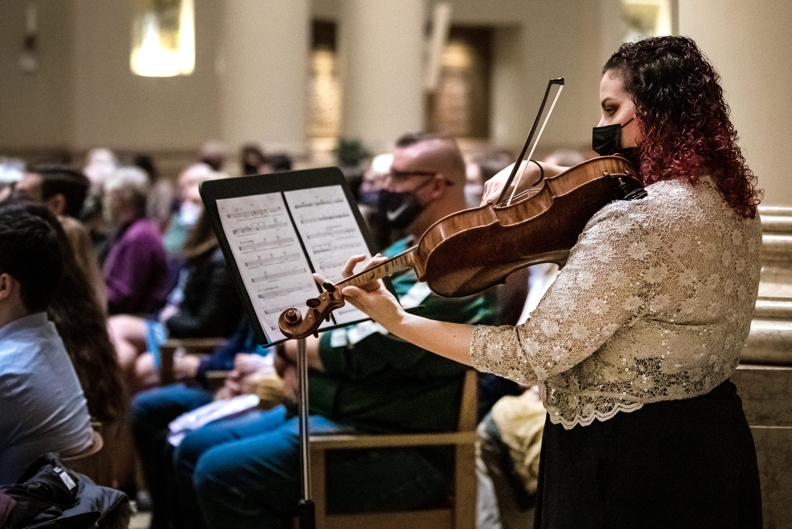 A woman plays a viola among the crowd listening to a performance in a church
