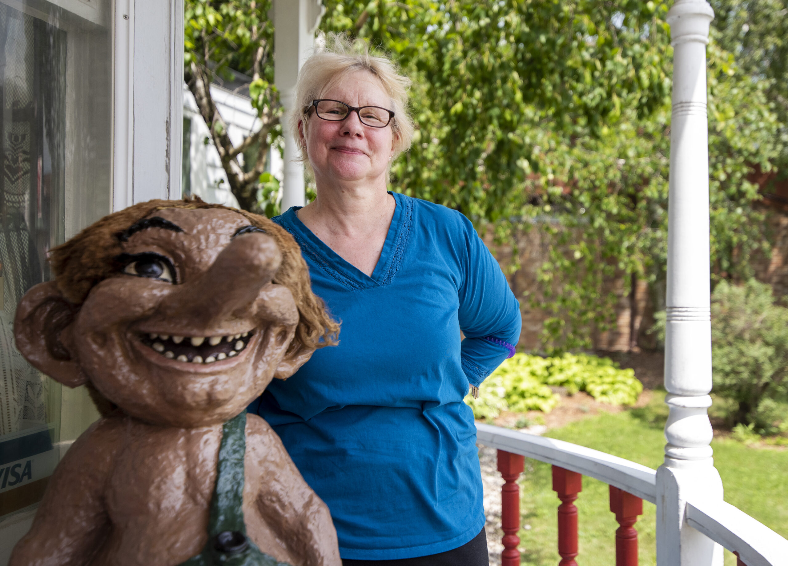 A woman stands next to a troll statue with a large nose.