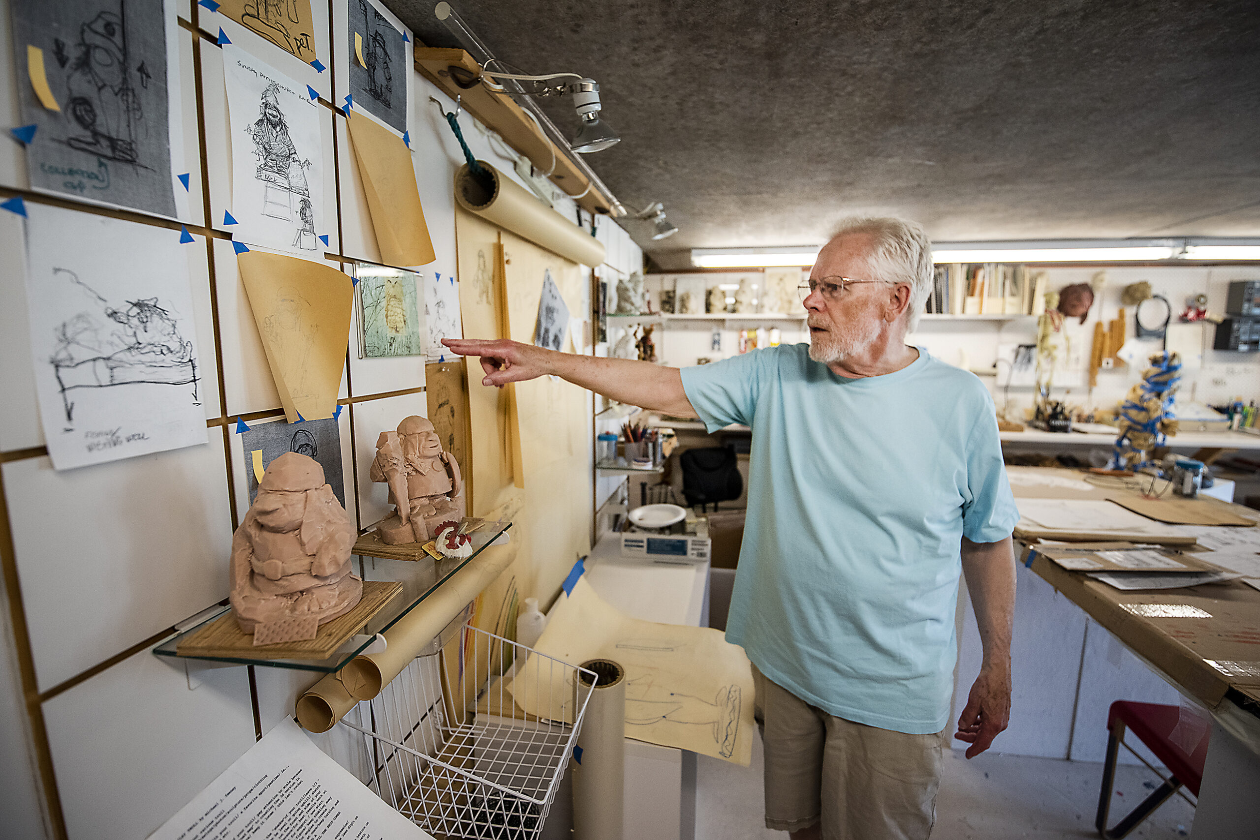 An artist points at many sketches pinned up around his studio.