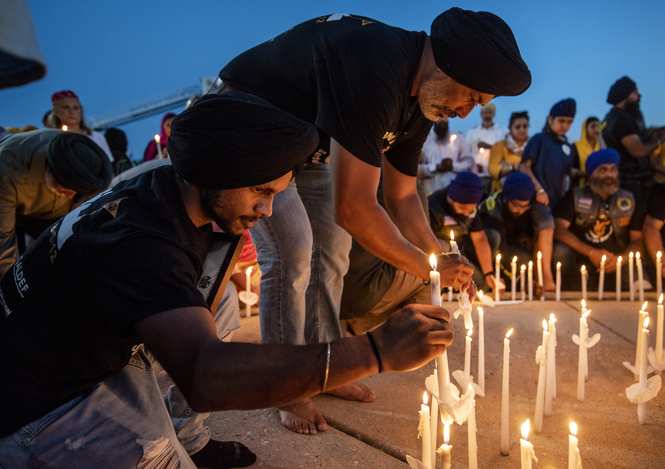 Two men lean down to place candles on the ground.