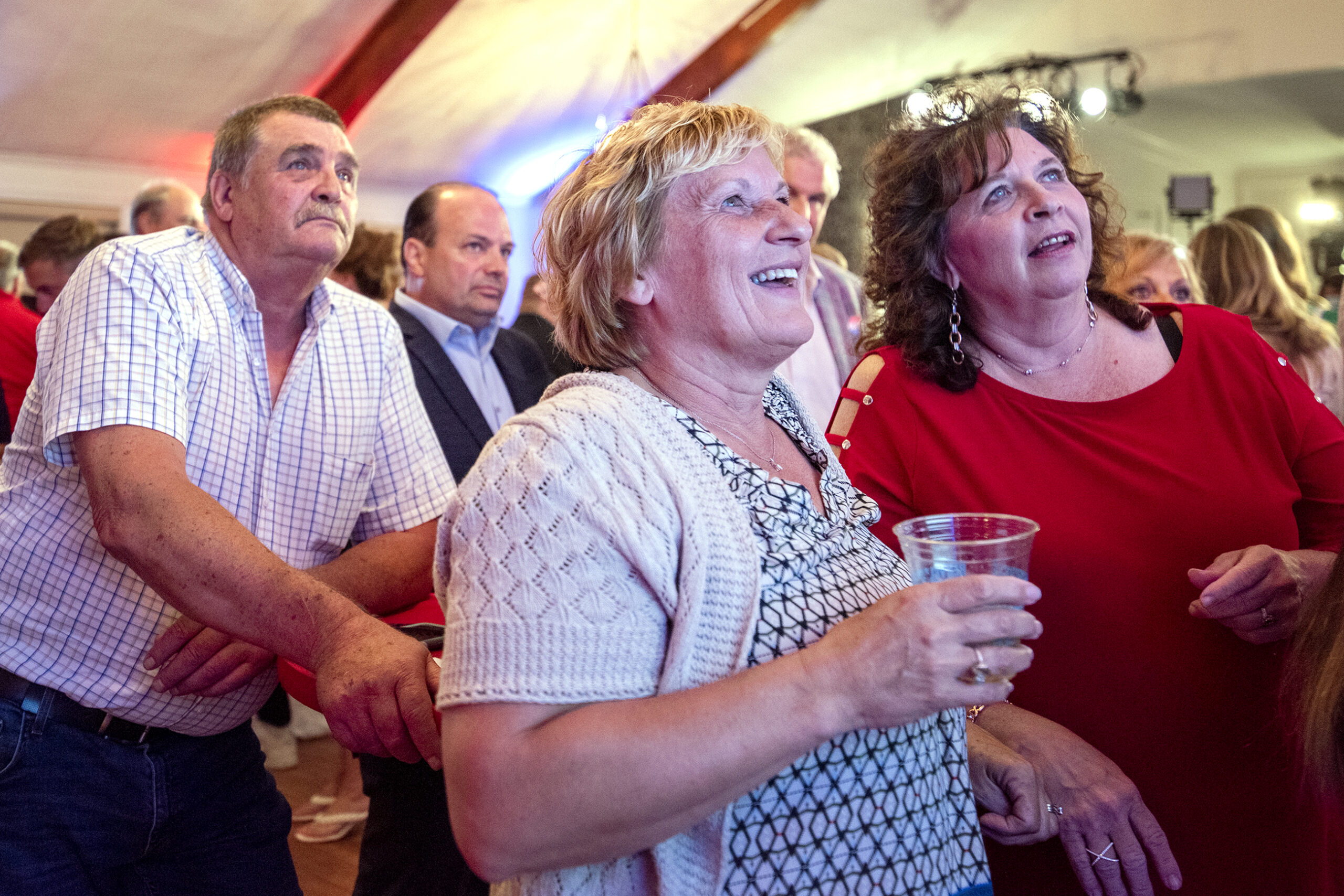 Tim Michels supporters watch with excitement as results appear on a tv screen.