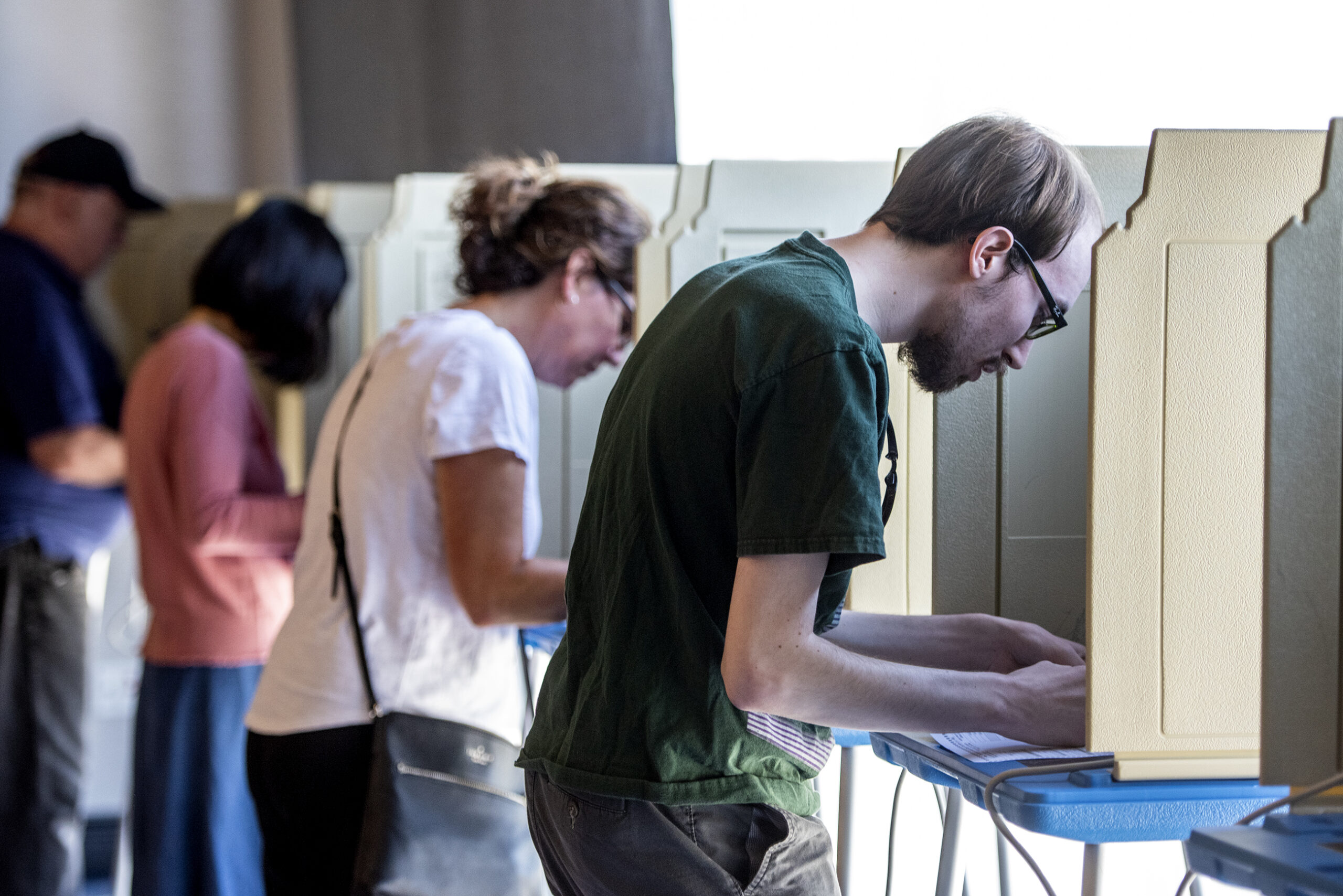 Four people lean forward as they vote in booths.