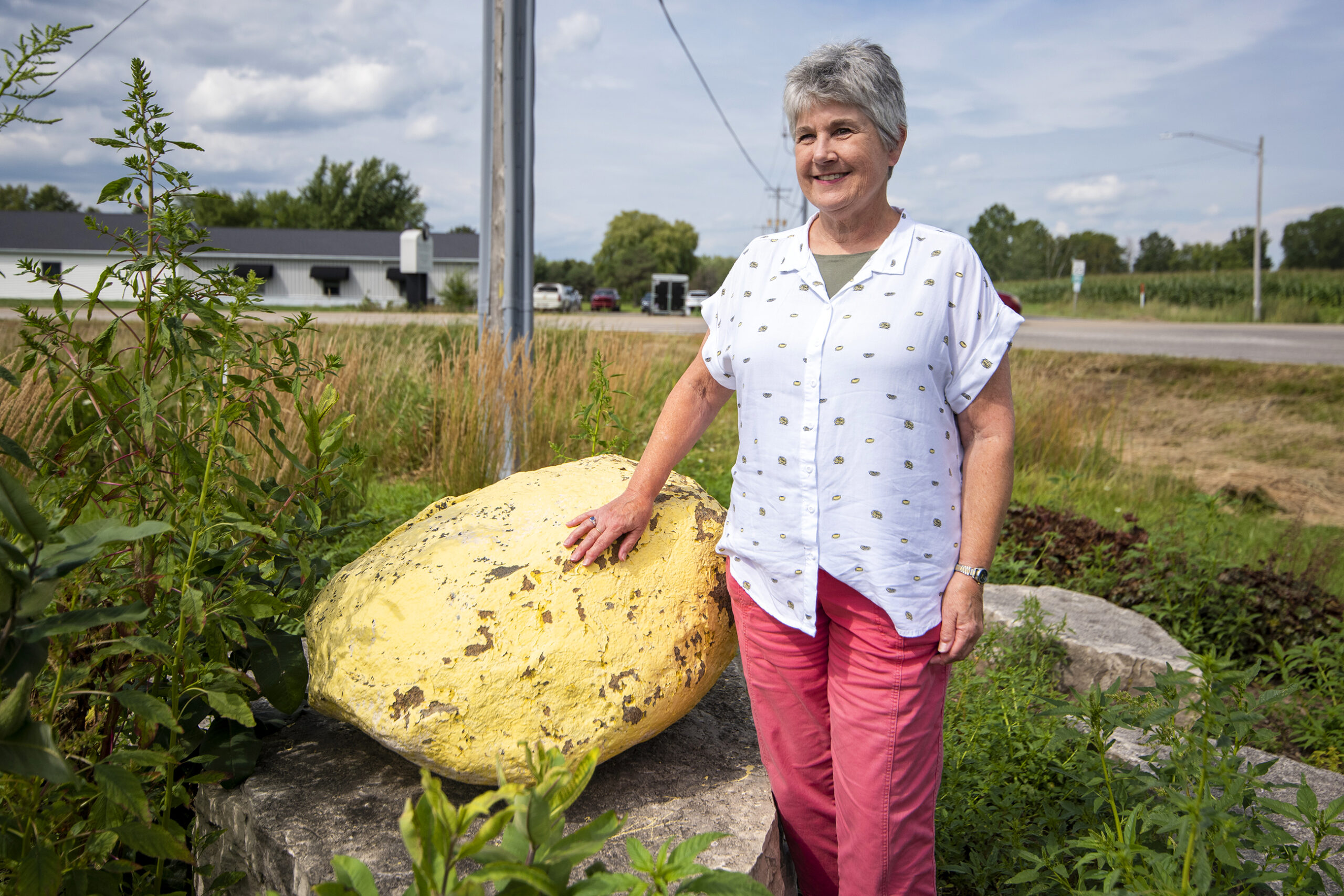 Beth English stands near a large boulder painted yellow.