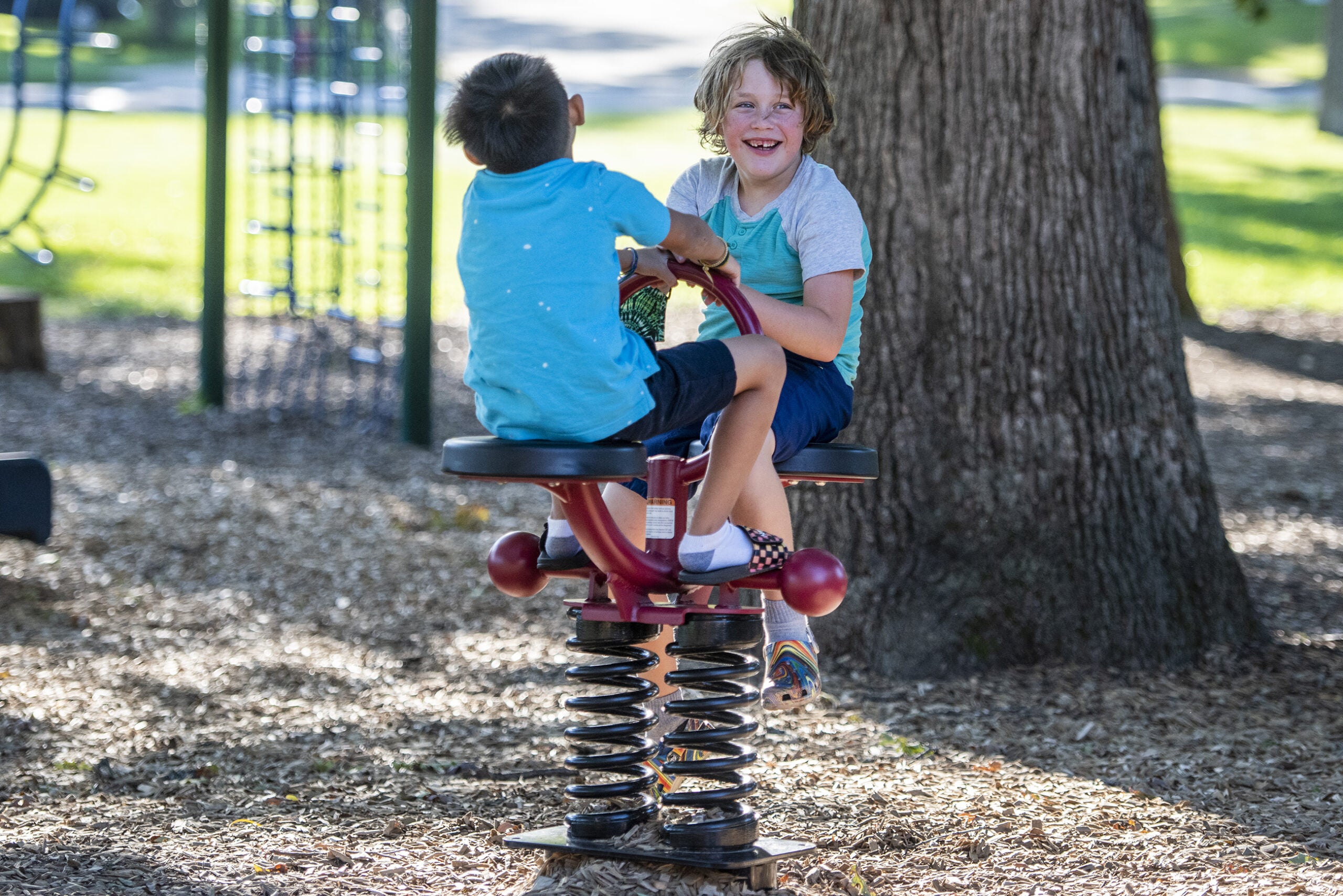 Two children sit on a bouncy piece of playground equipment.