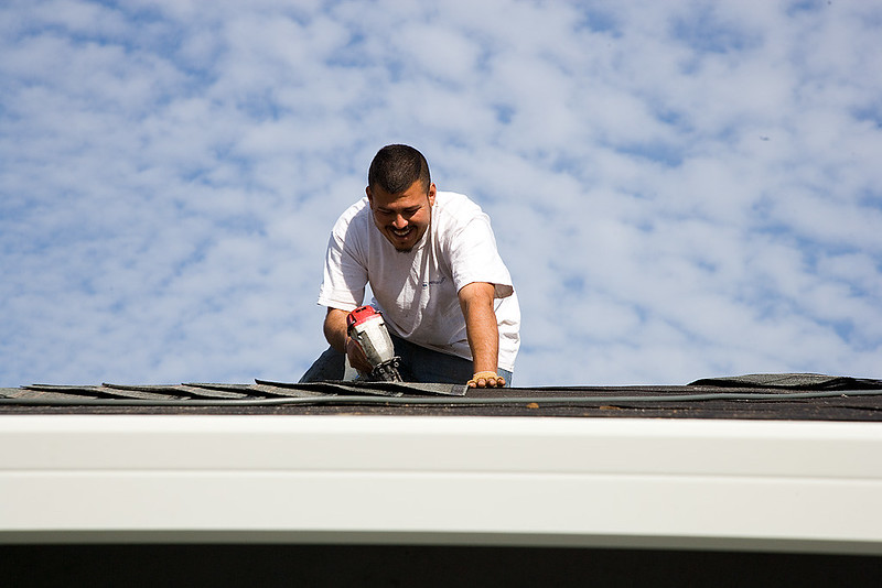 A person instals shingles on a roof of a house.