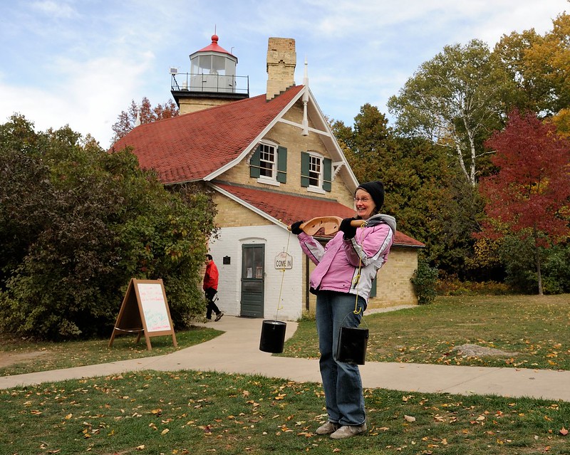 Person carries water pails in front of lighthouse