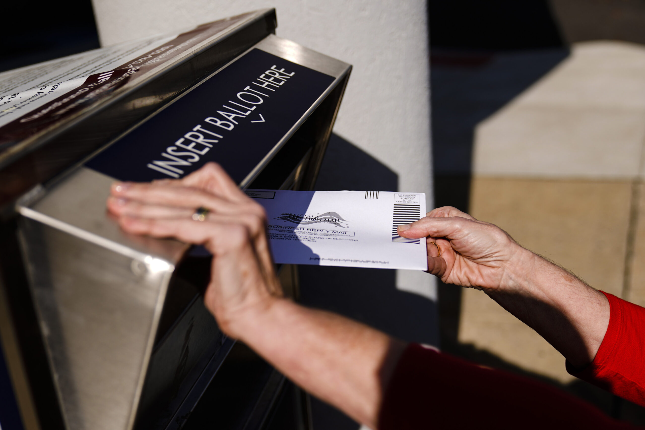A person drops off a mail-in ballot at an election ballot return box
