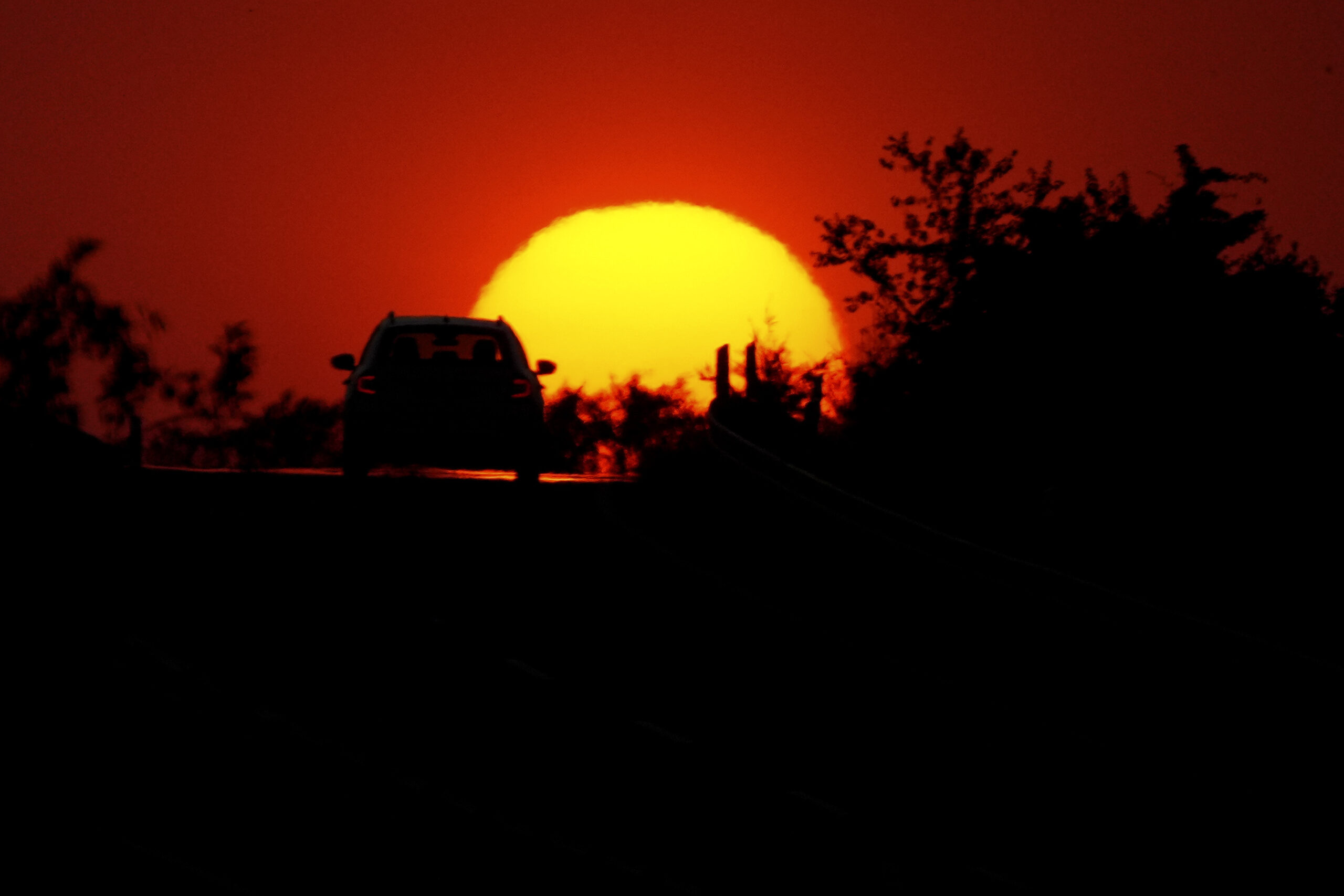 Bright yellow sun sets in orange sky as car drives