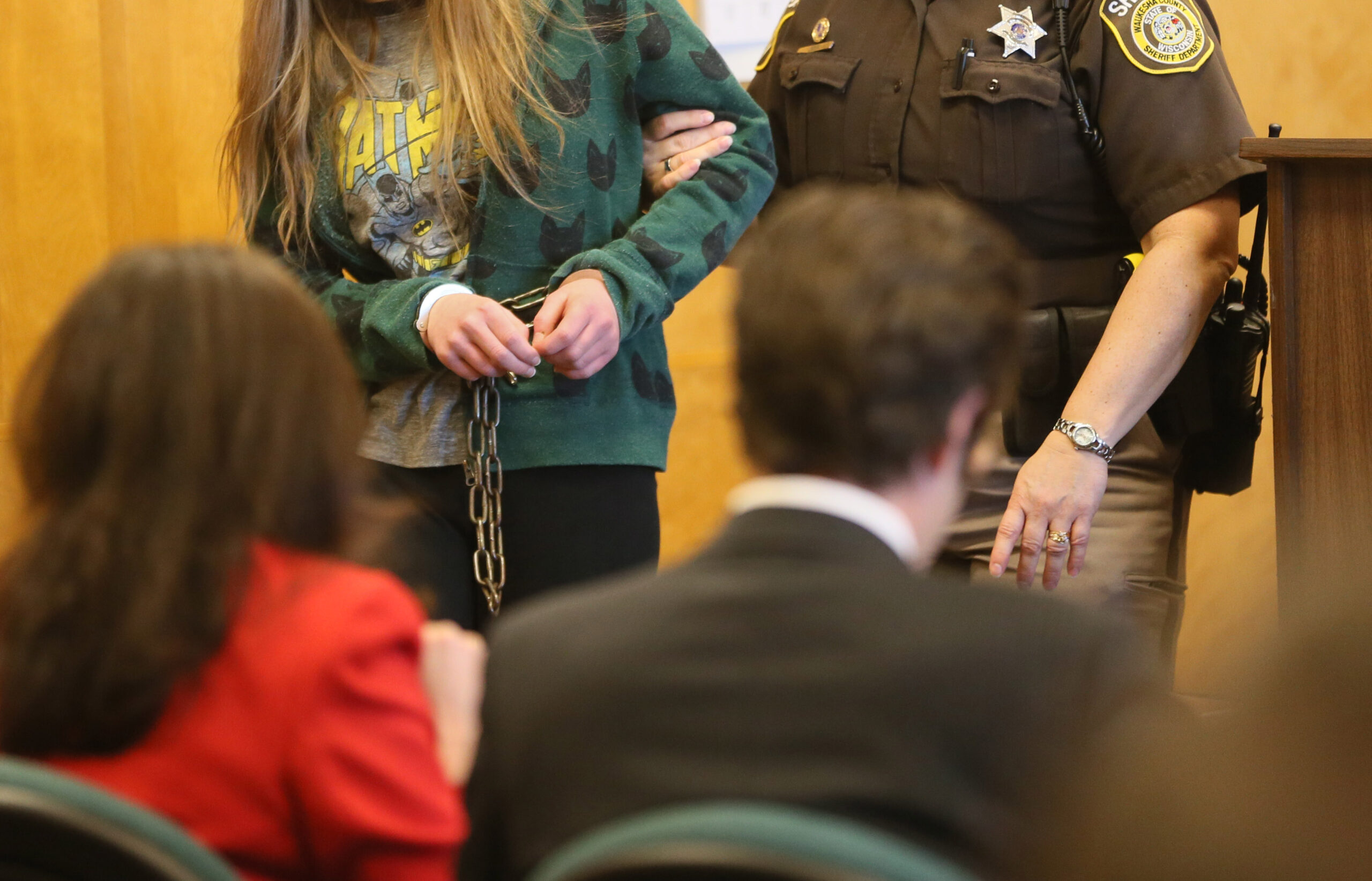 A girl being led into a courtroom by an officer