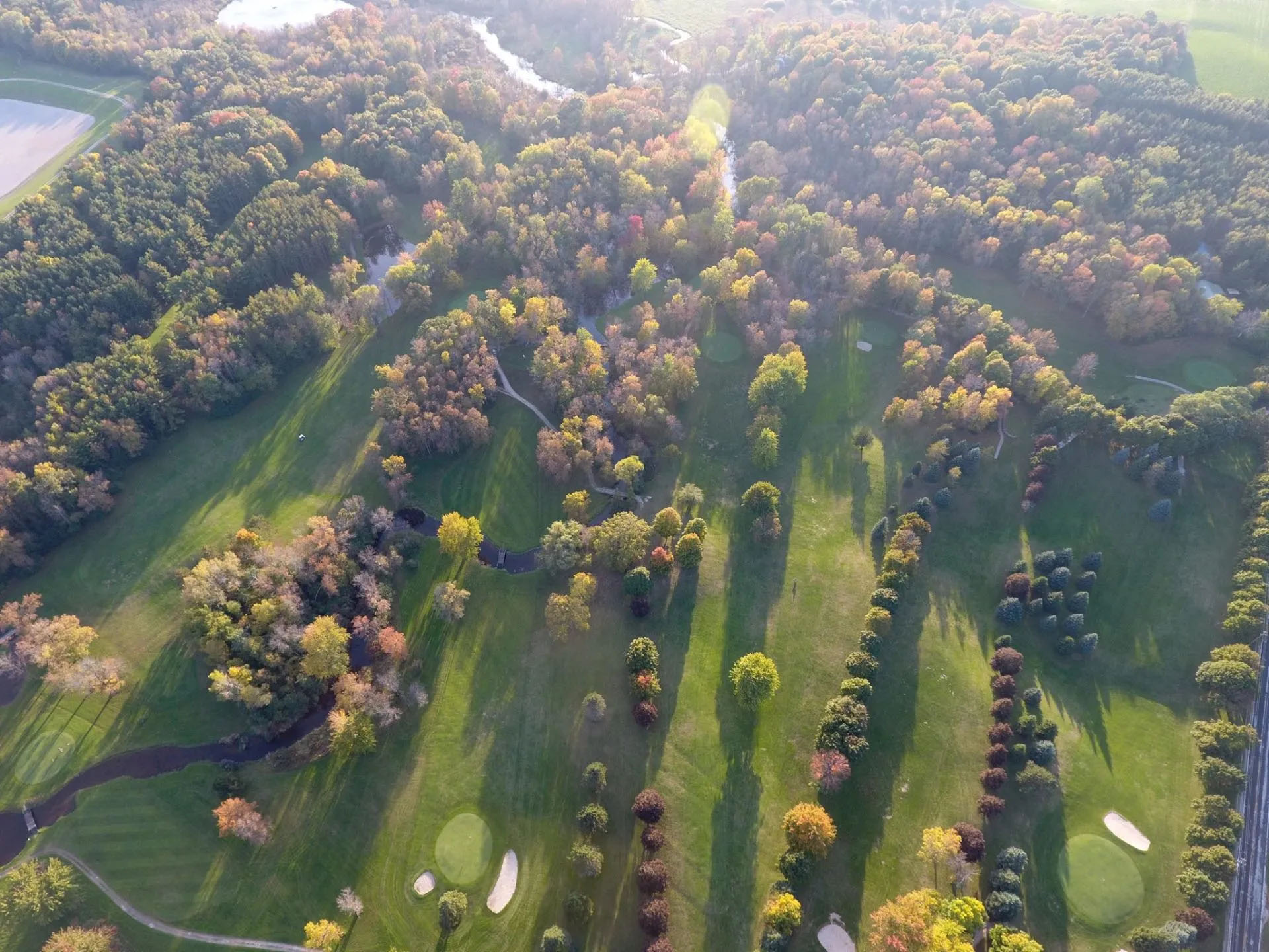 An aerial view of a golf course, showing some greens and surrounding trees