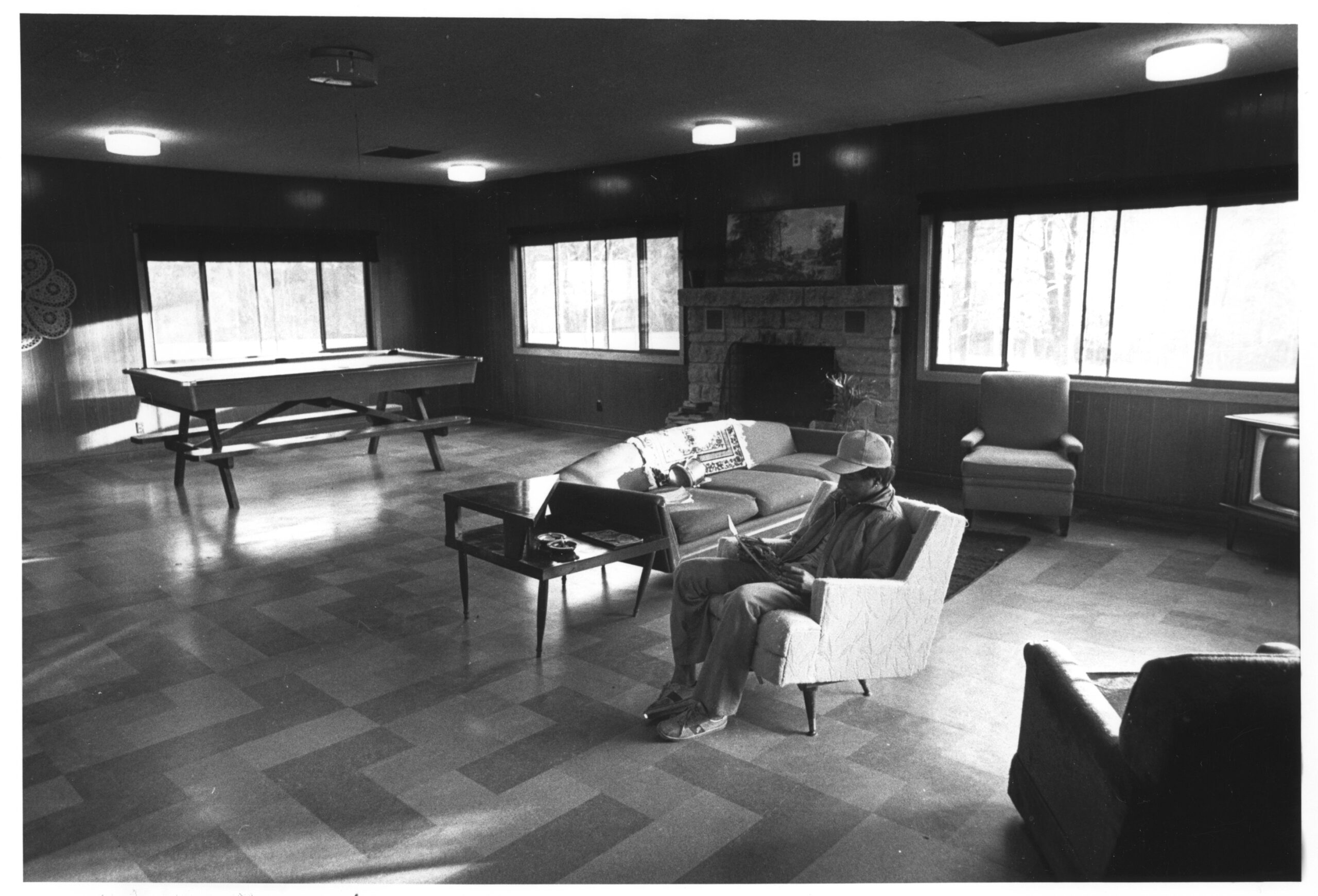 A black and white photograph featuring an unidentified refugee sitting in the recreation room of the Wyalusing compund
