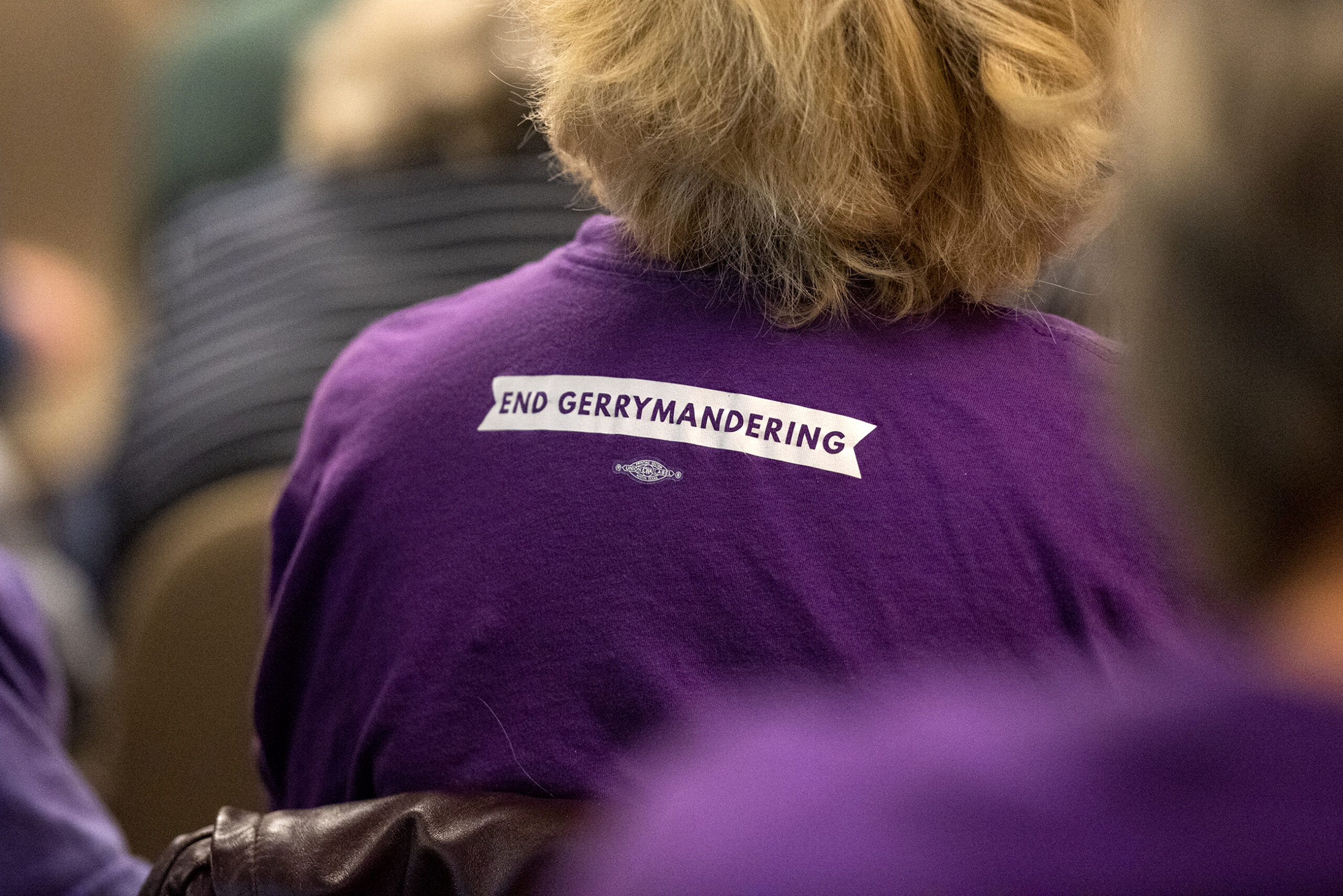 An attendee wears a purple shirt that says "end gerrymandering" on the back.
