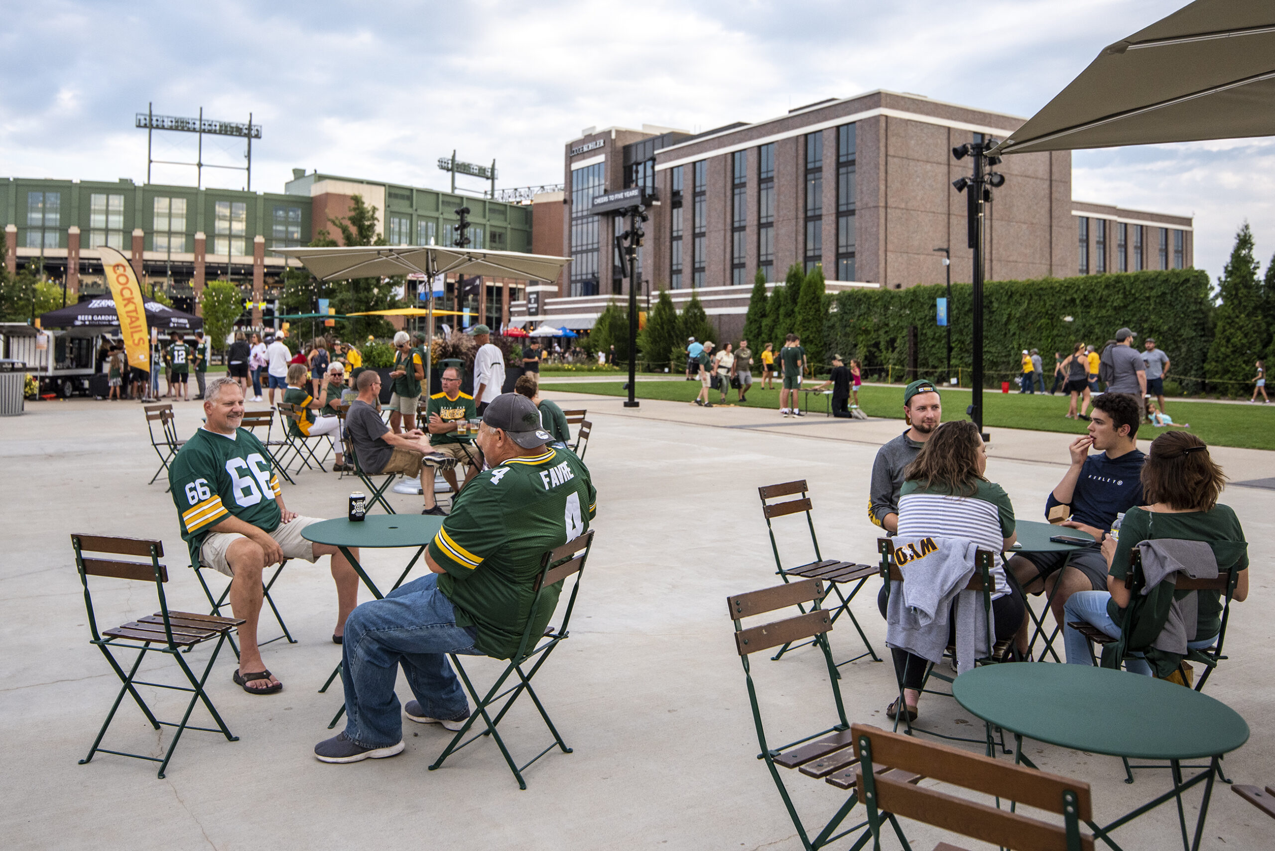 Fans in Packers gear drink beer at tables set up near the stadium.