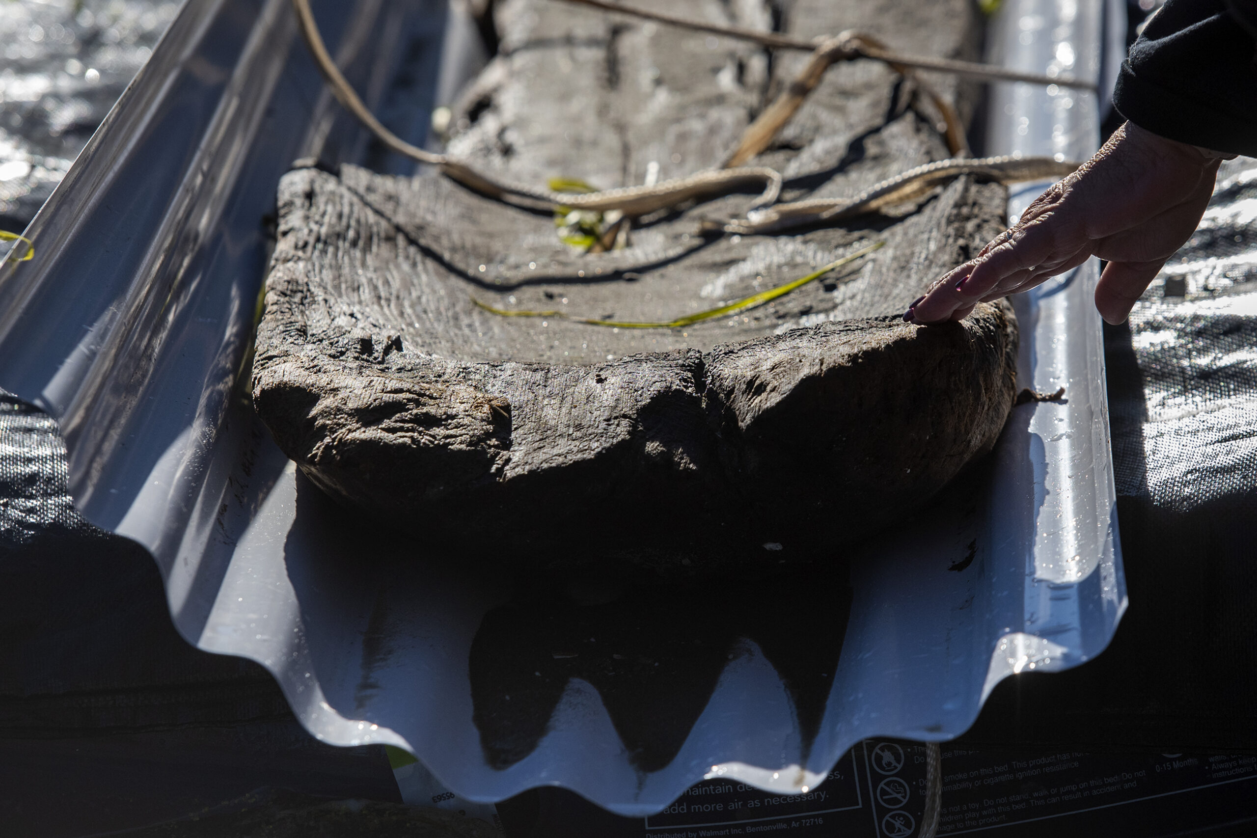 A hand touches the aged wood of a canoe.