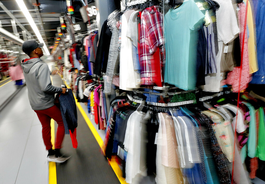 A man selects a top from long double racks of clothing in a warehouse.