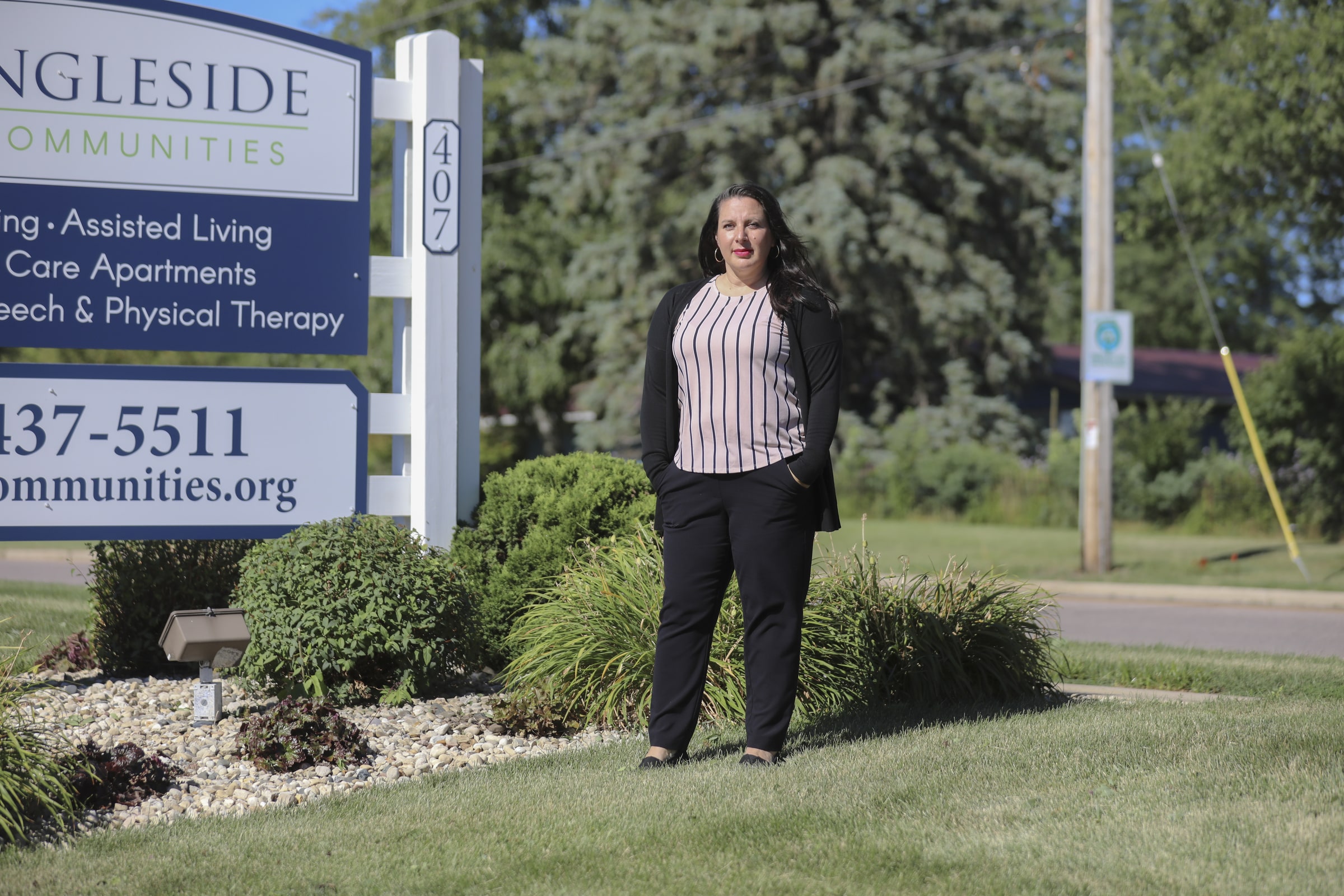 Danielle Sigler poses in front of the sign of Ingleside Communities in Mount Horeb, Wis., where she works