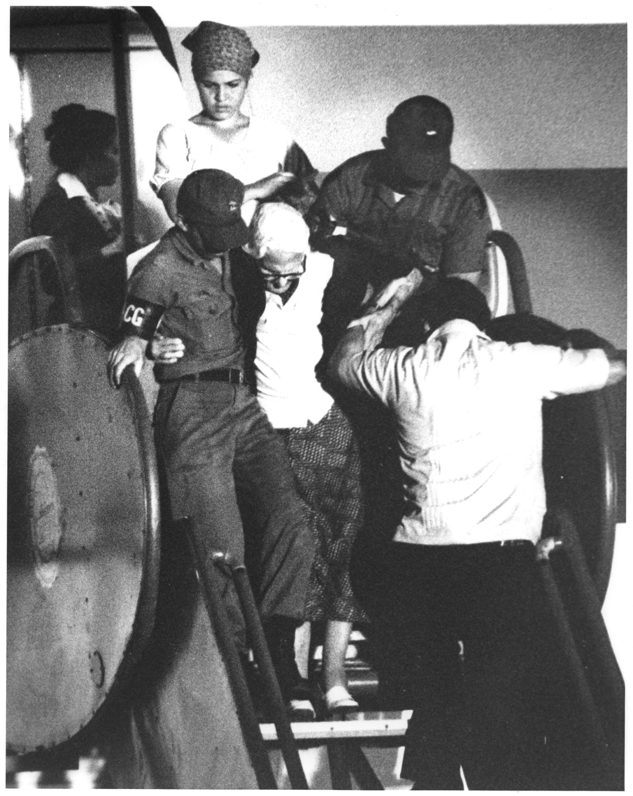 A black and white photograph featuring an elderly refugee being assisted deplaning