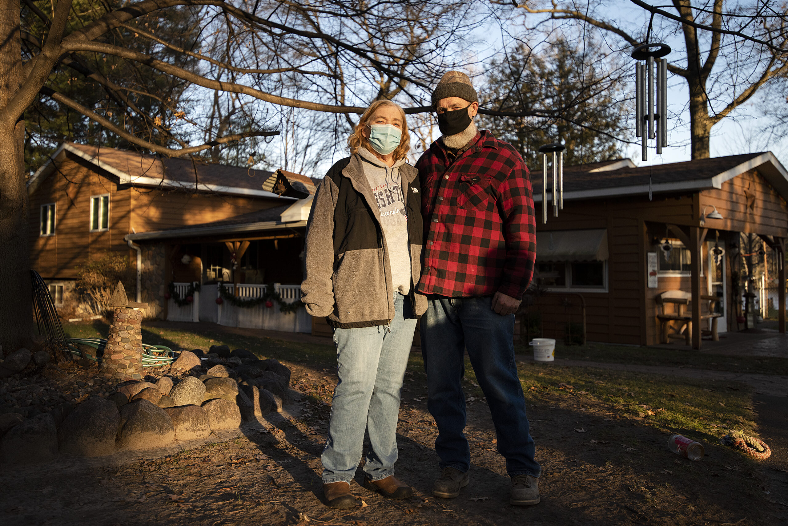 A couple wears face masks as they stand outside in their lawn