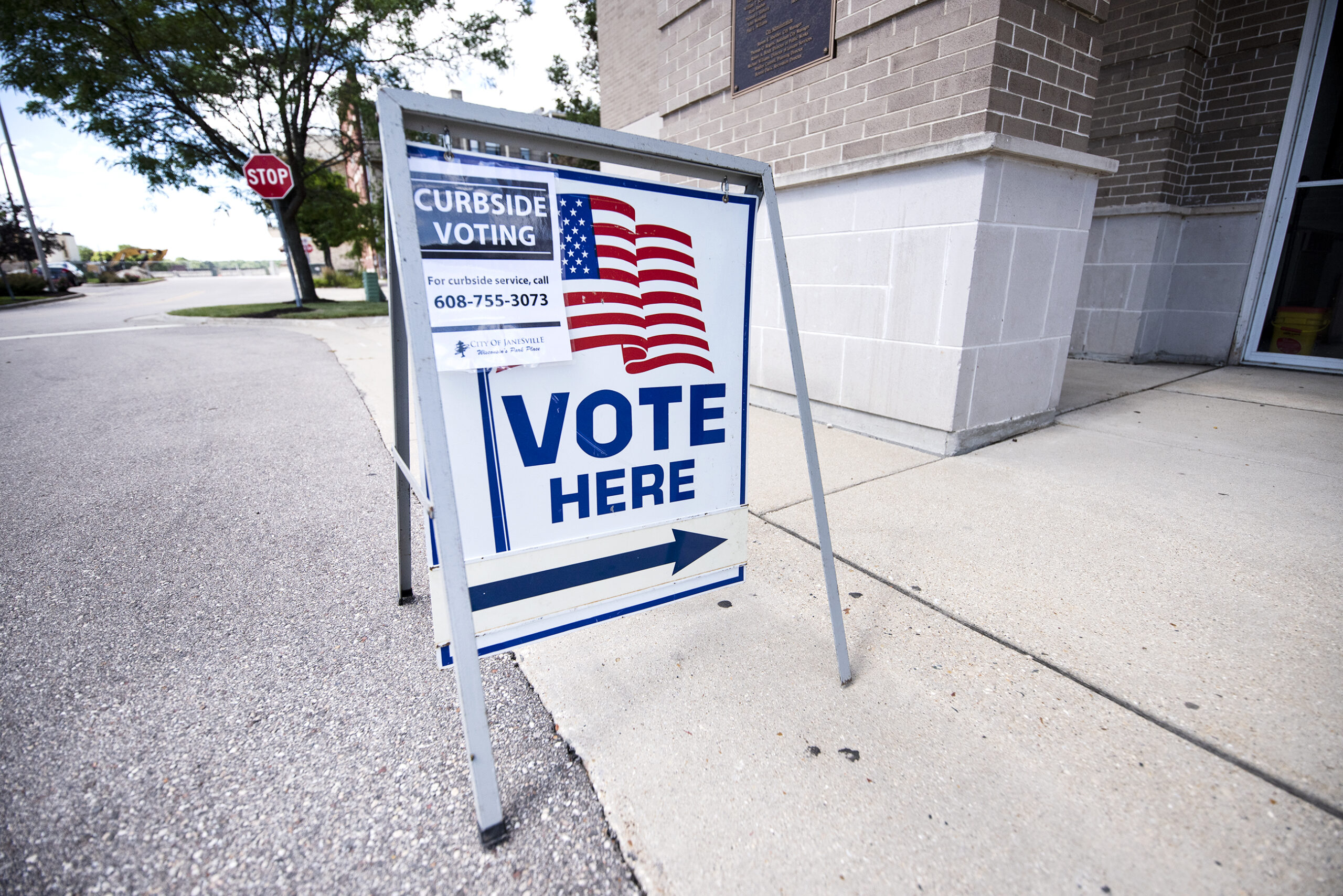 A "Vote Here" sign has an added sign about curbside voting