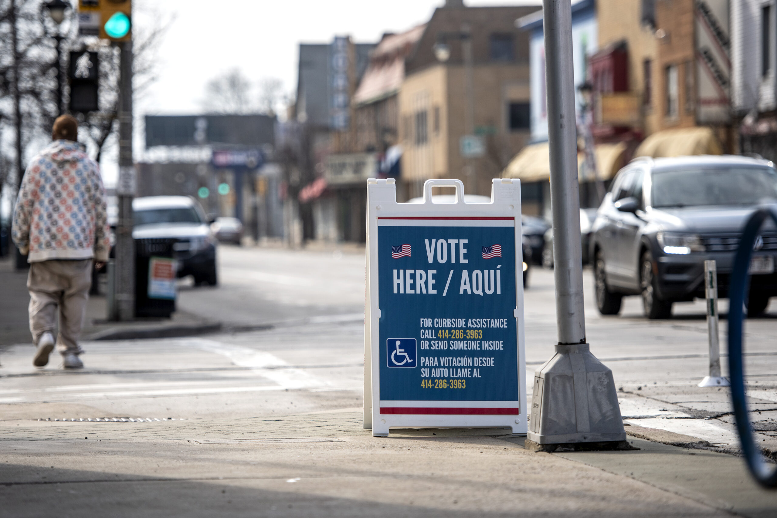 The sun shines on an outdoor sign that says "Vote Here" in English and in Spanish.