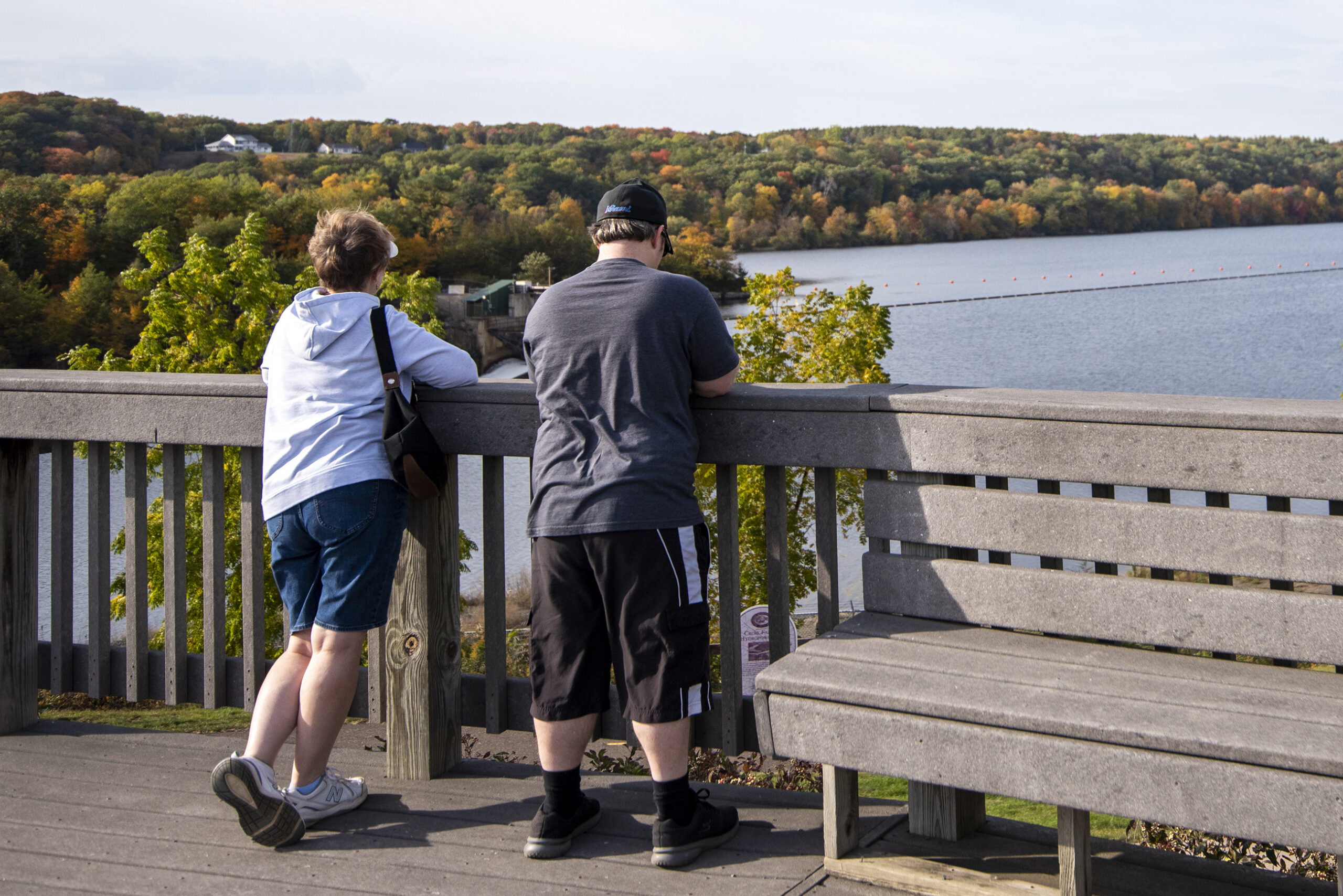 Two sight-seers lean on a railing overlooking a river and trees.