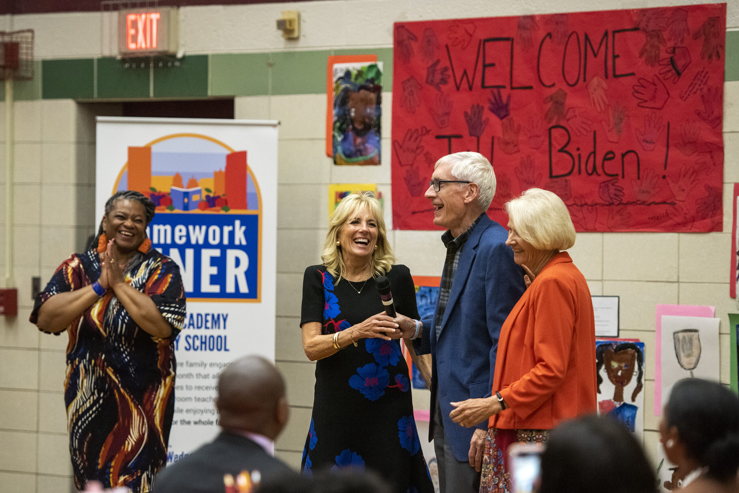 First lady Jill Biden, Gov. Tony Evers and Wisconsin First lady Kathy Evers laugh together at the front of an elementary school gymnasium.
