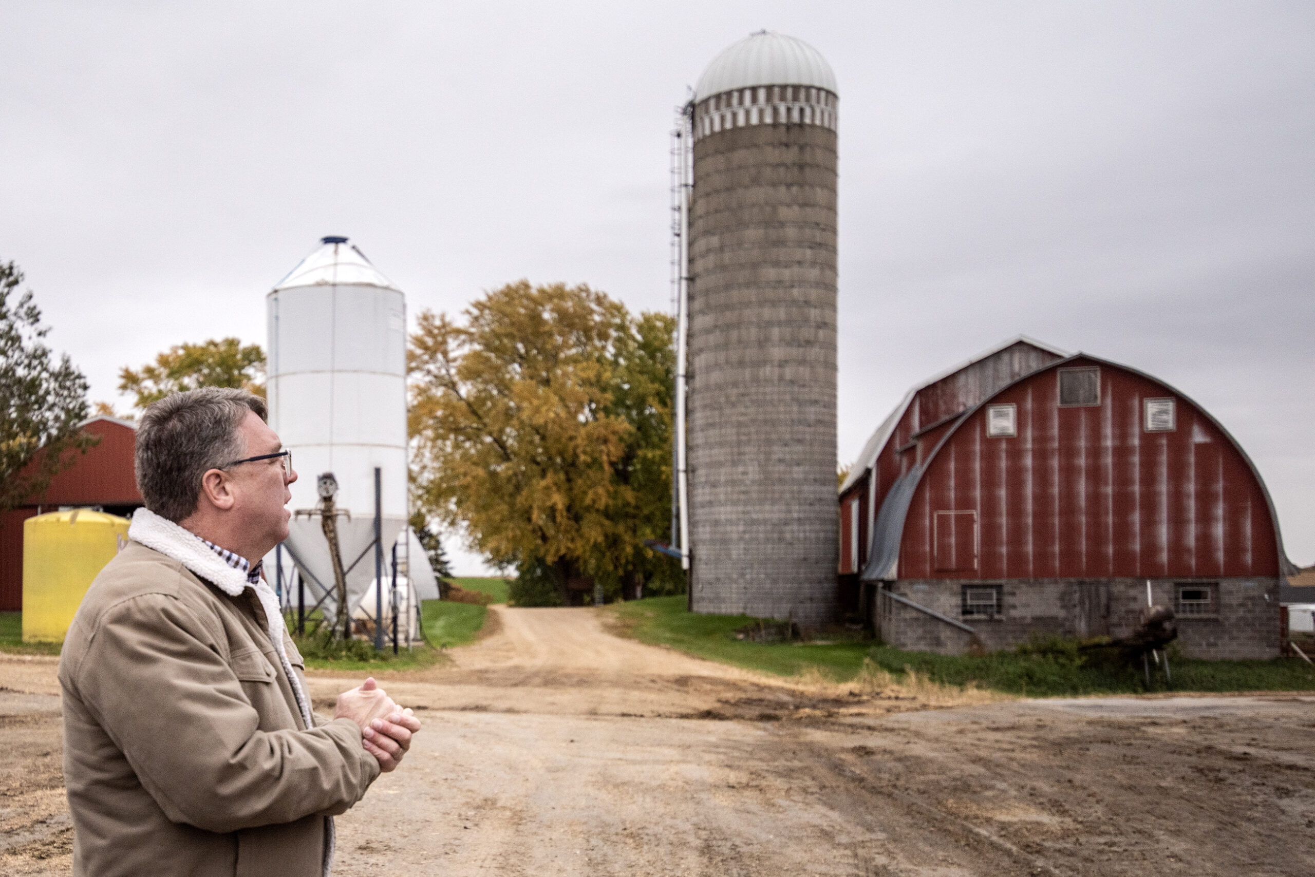Brad Pfaff stands outside in front of a red barn and old silo.