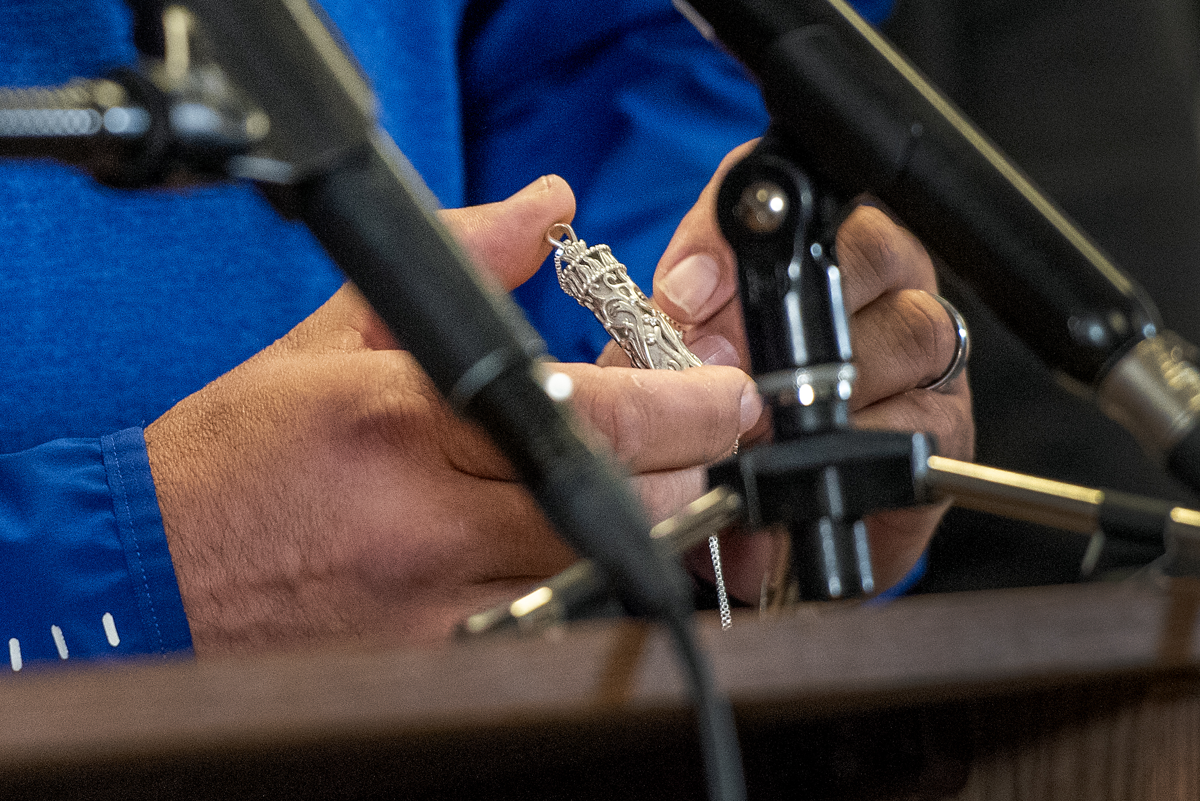 A small silver container with ornate detail is held in the hands of a man speaking at a podium during a press conference.