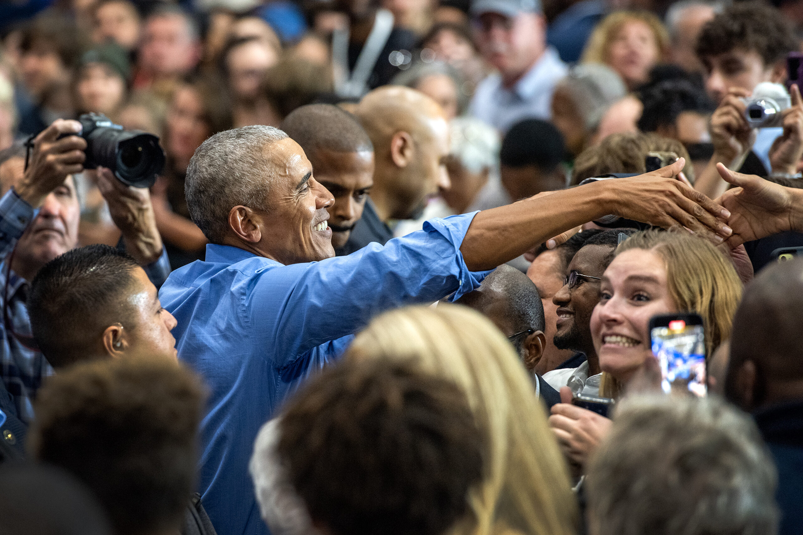 Former President Barack Obama reaches over a crowd of people to shake hands.