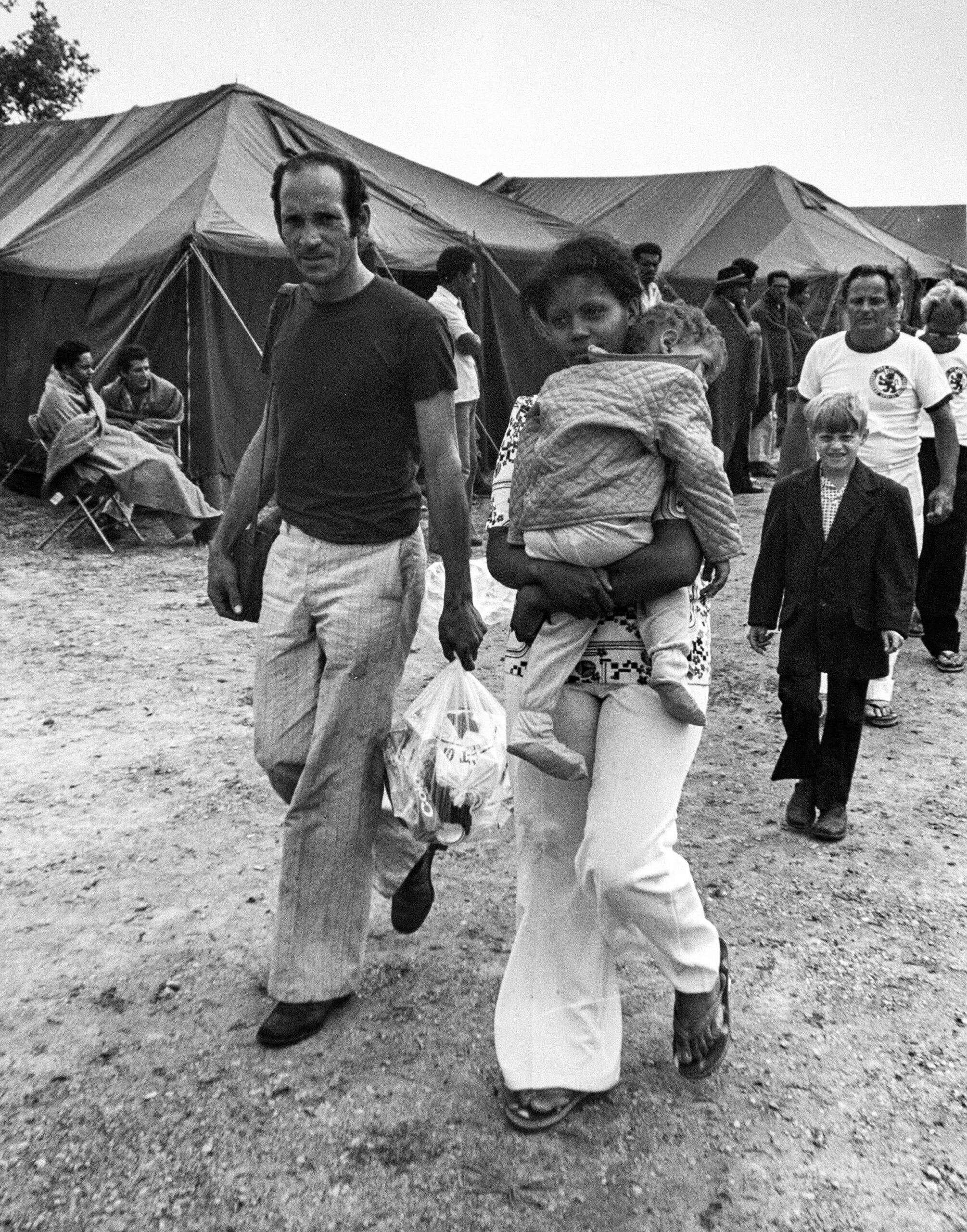 A couple walks from a tent at Fort McCoy, with the wife holding their daughter