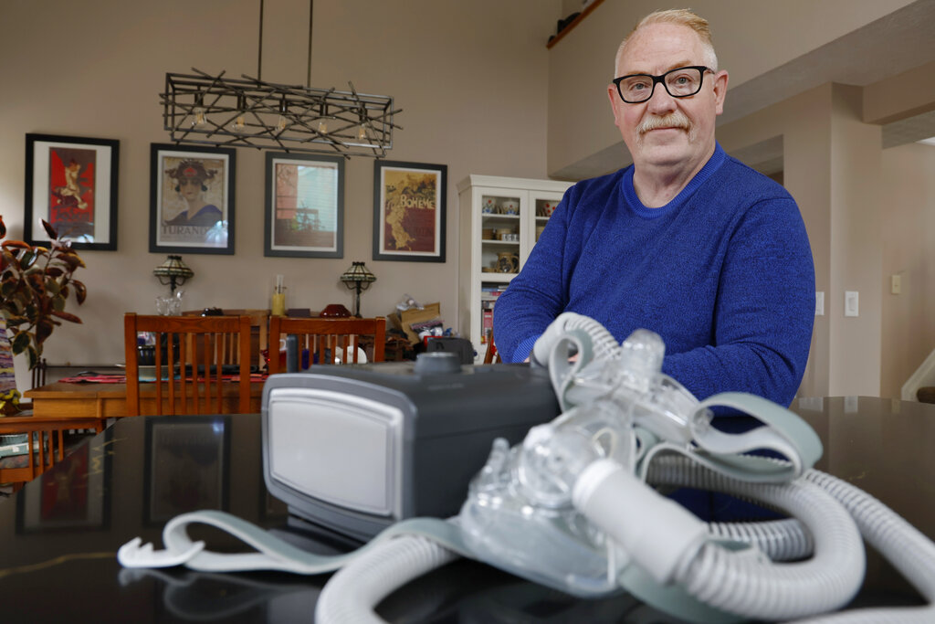 Jeffrey Reed, who experienced persistent sinus infections and two bouts of pneumonia while using a Philips CPAP machine, poses with the device at his home.