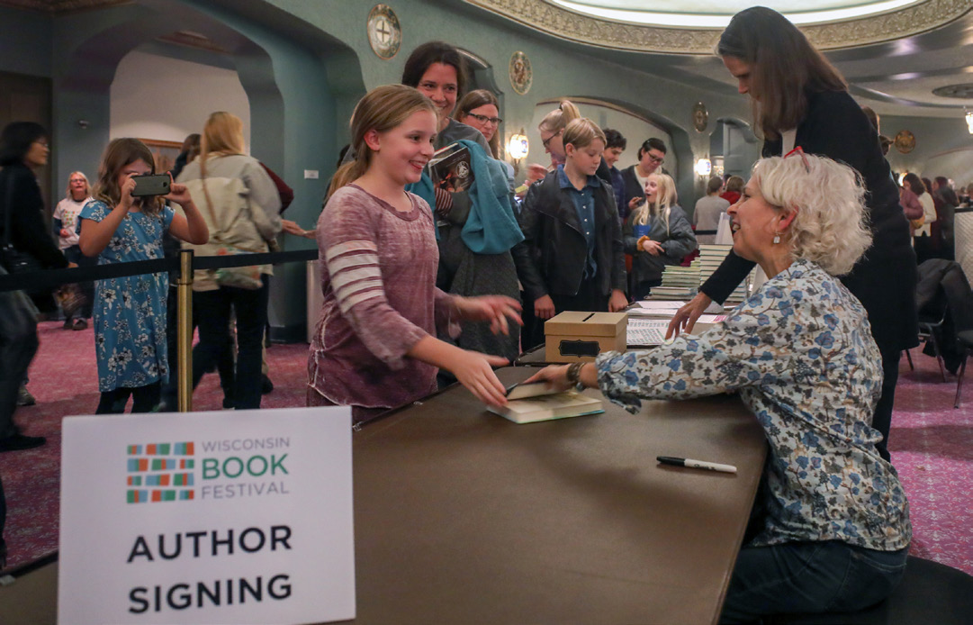 A girl hands a book to an author to be signed at a book festival.
