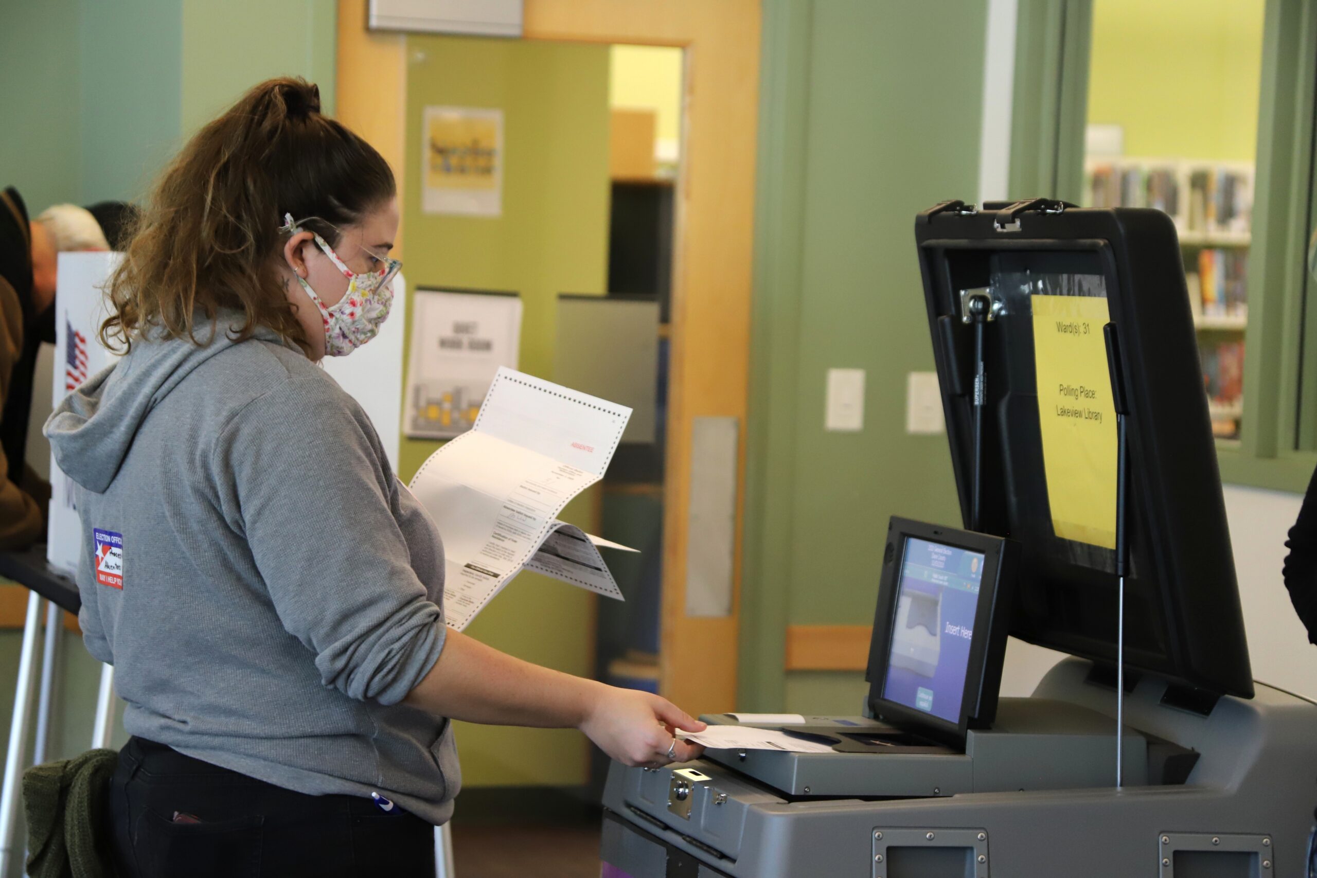 A poll worker inserting absentee ballots into a voting machine at the Lakeview Library on Madison's north side