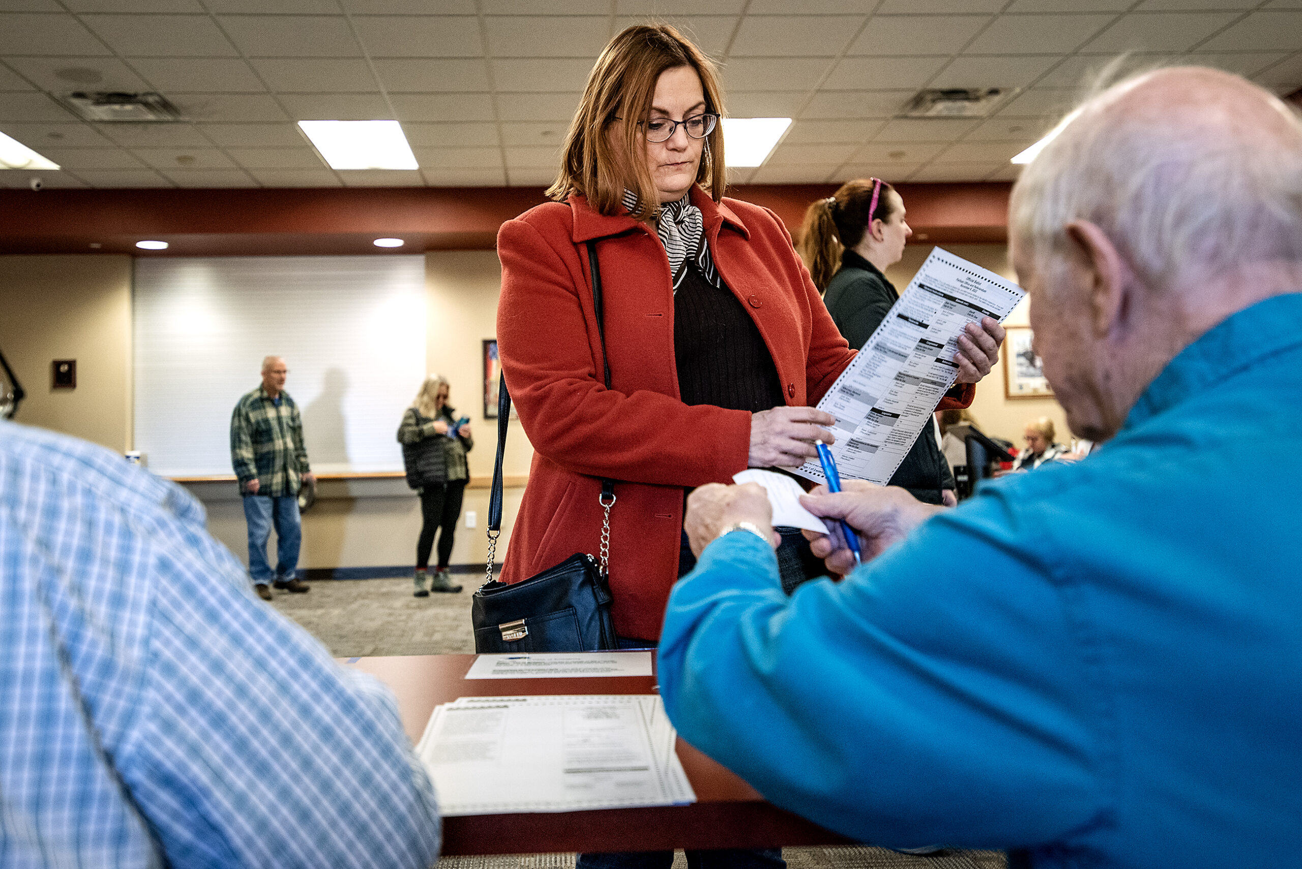 A voter in a red coat holds a ballot.