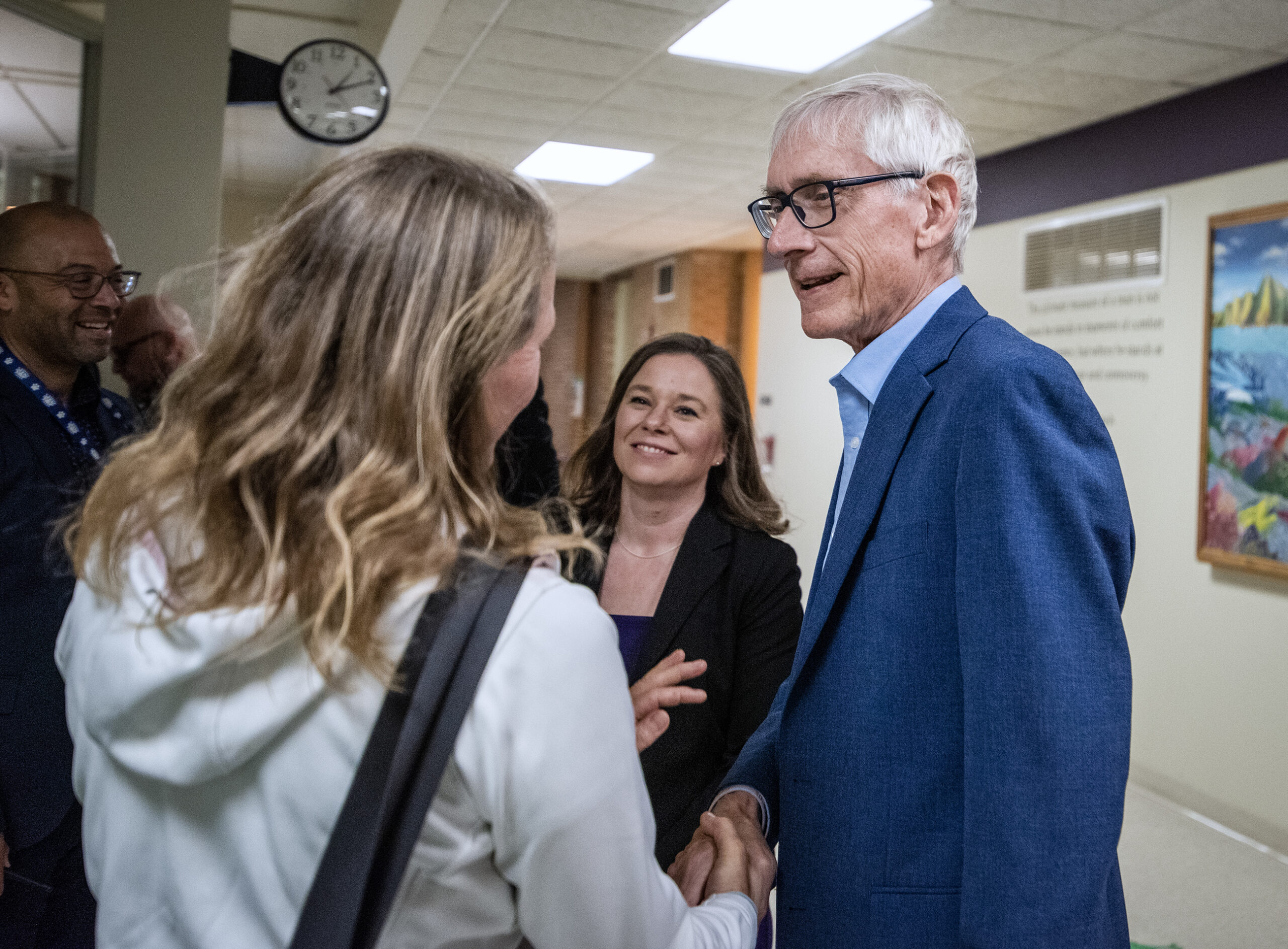 Gov. Tony Evers and Lt. Gov.-elect Rodriguez speak to a person in a school hallway.