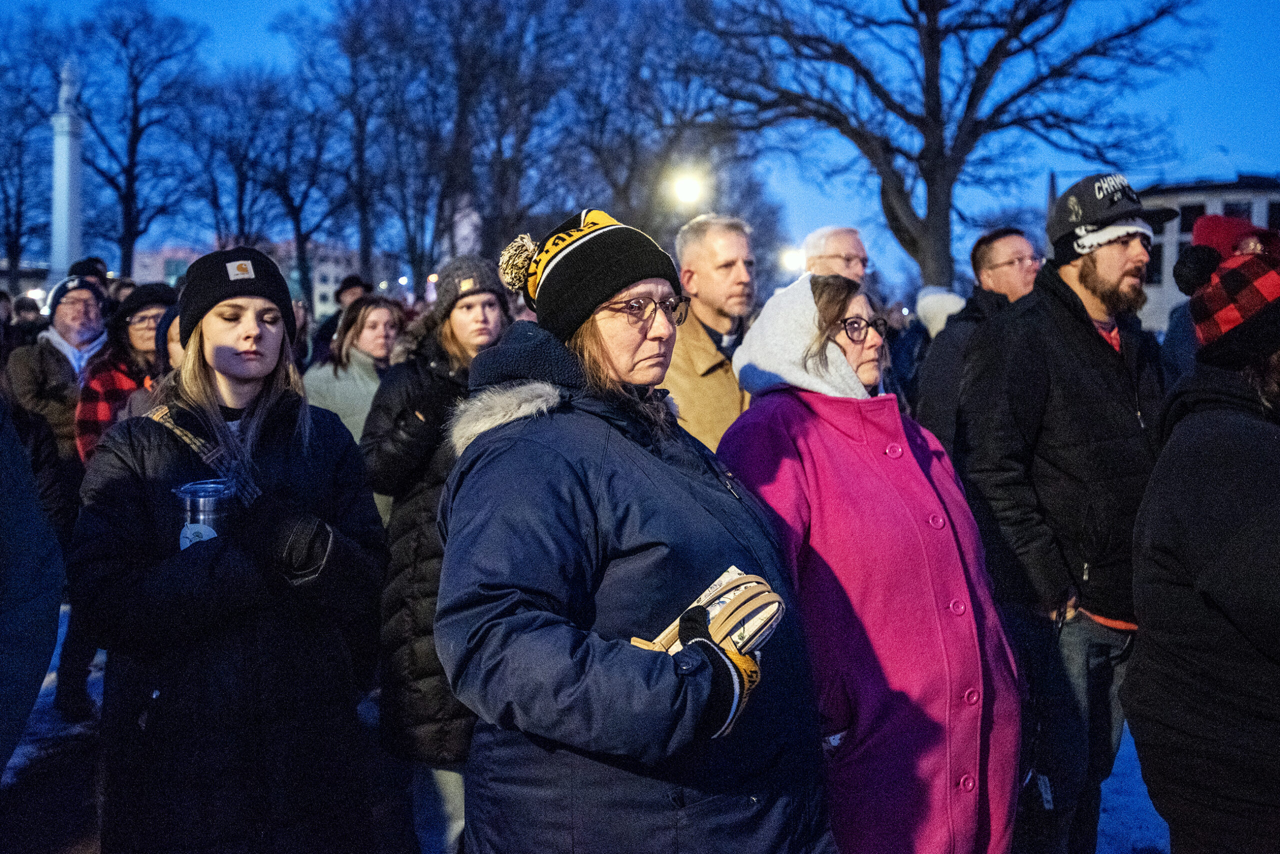 People in winter coats stand together at dusk.