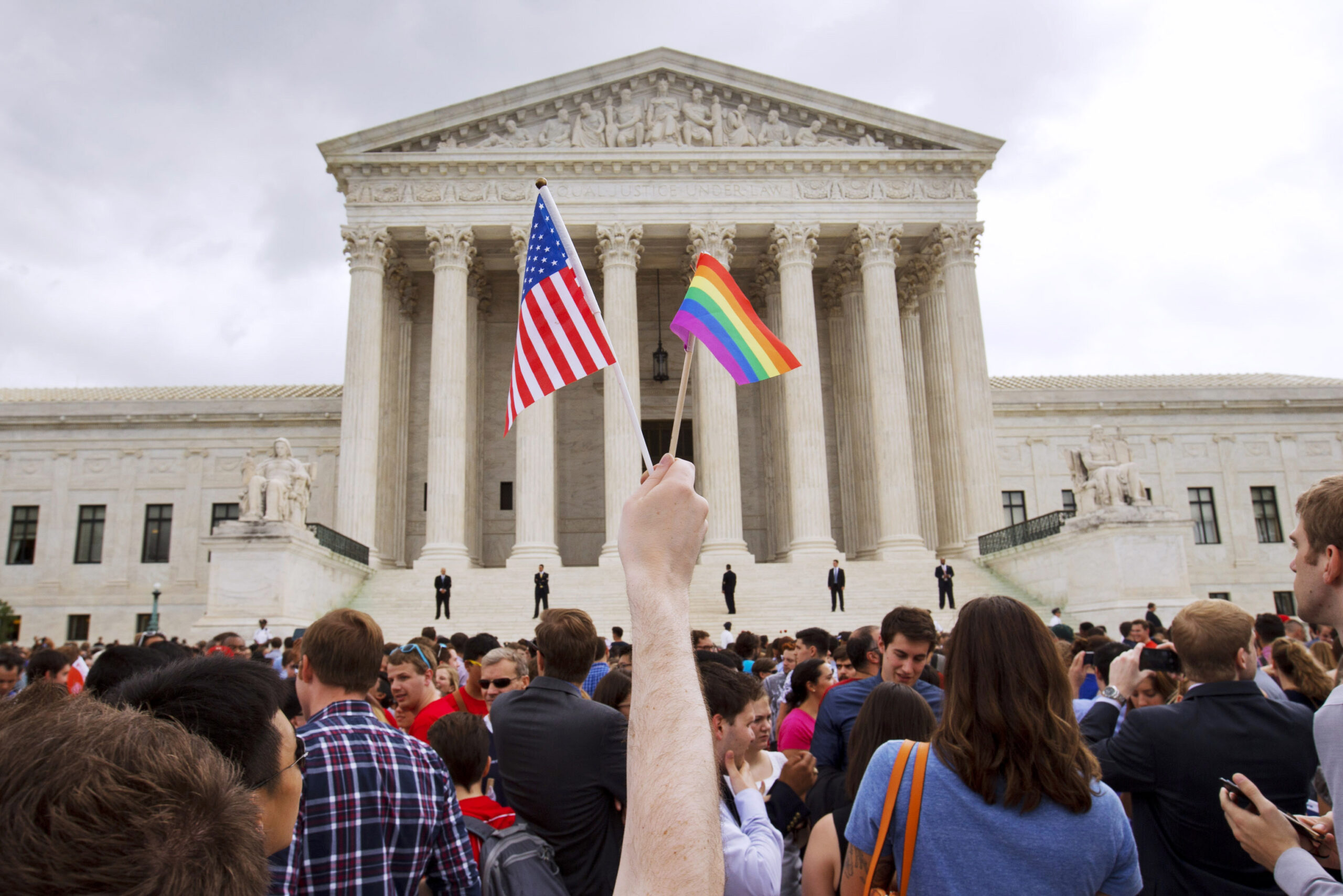 A man holds a U.S. and a rainbow flag outside the Supreme Court.