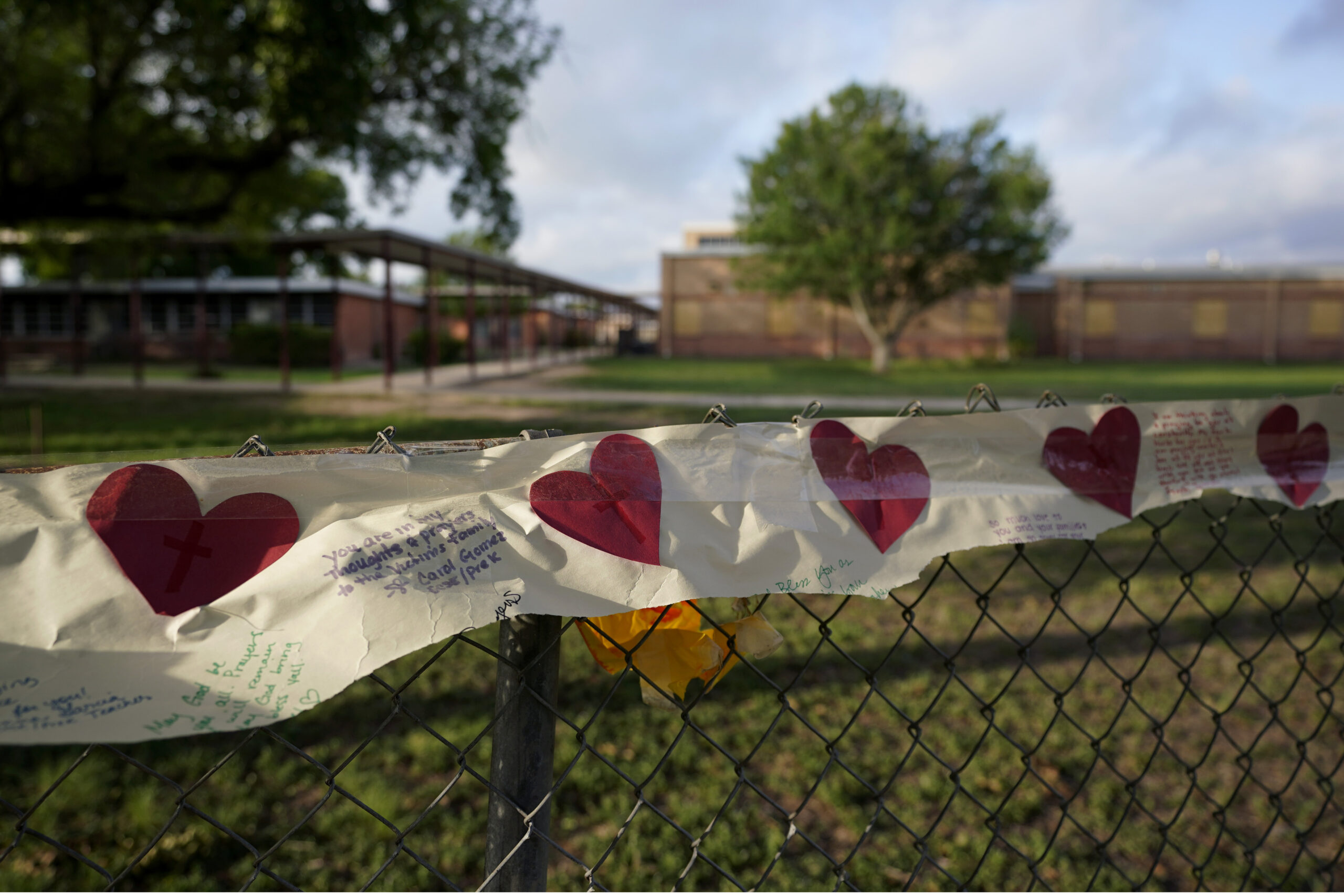 Hearts on a banner hang on a fence at a boarded up Robb Elementary School building where a memorial has been created to honor the victims killed in the recent school shooting