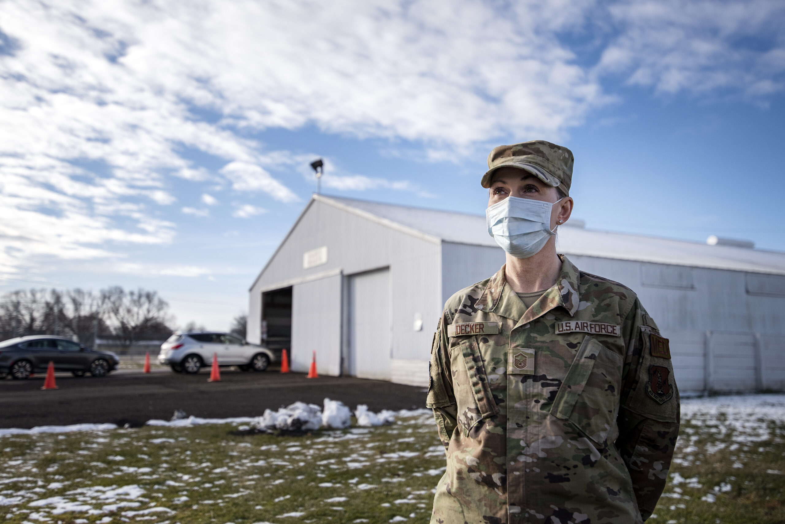 A woman in a military uniform stands near a barn that has been repurposed as a drive-thru testing site