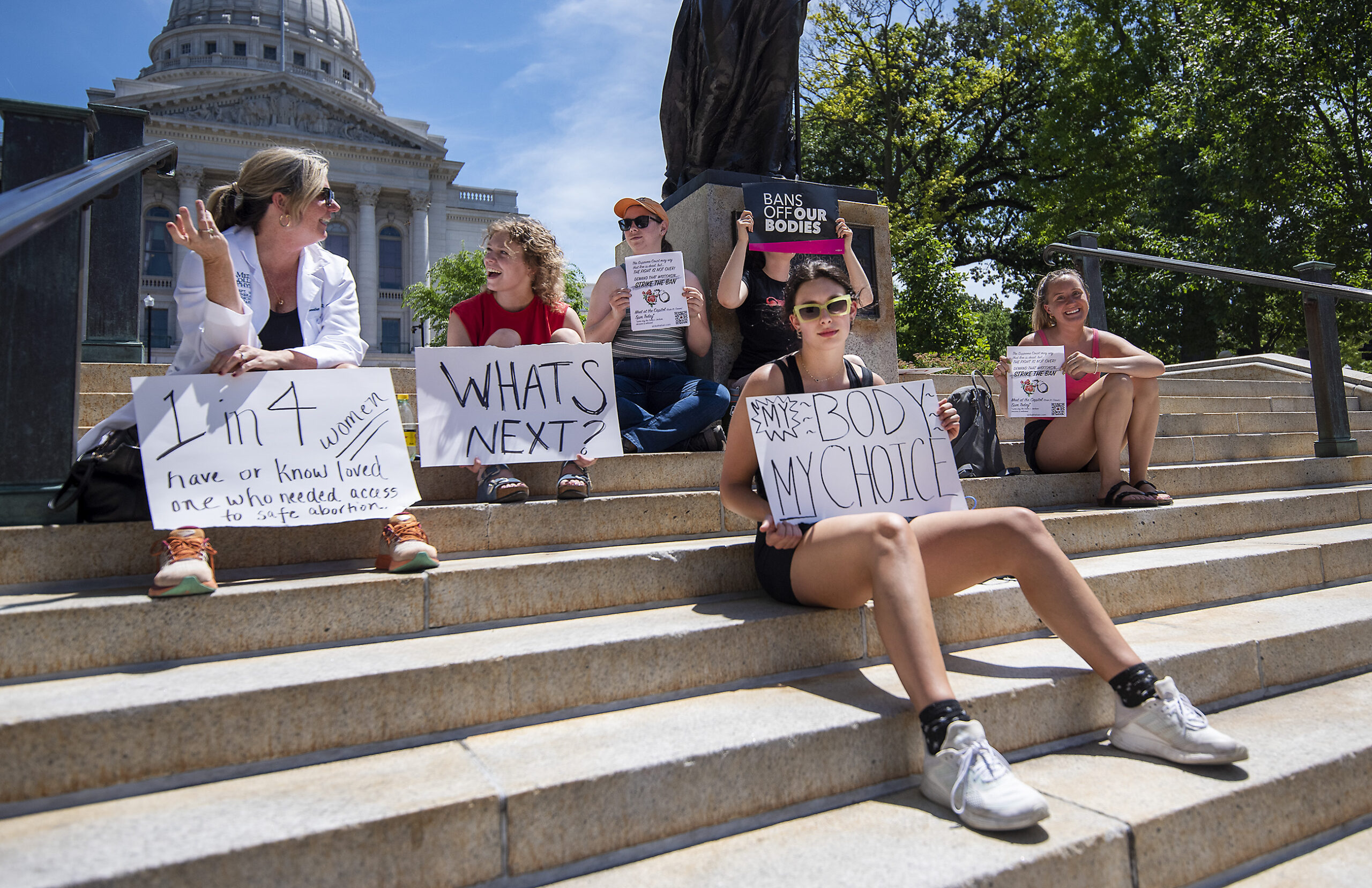 Six people hold poster board signs on the steps leading to the state capitol.