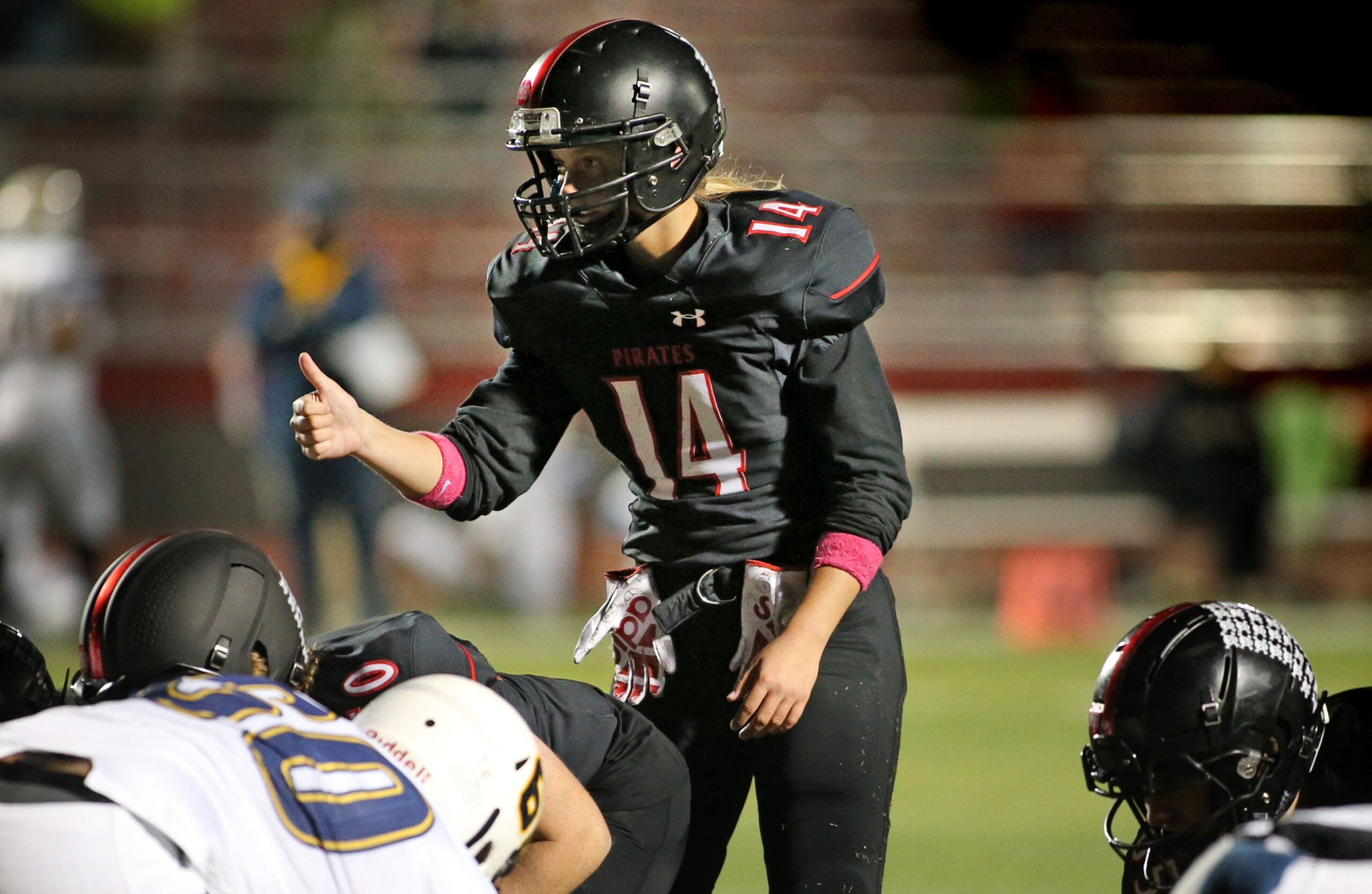 Ava Matz wears a black football uniform and helmet as she signals to teammates before a play.