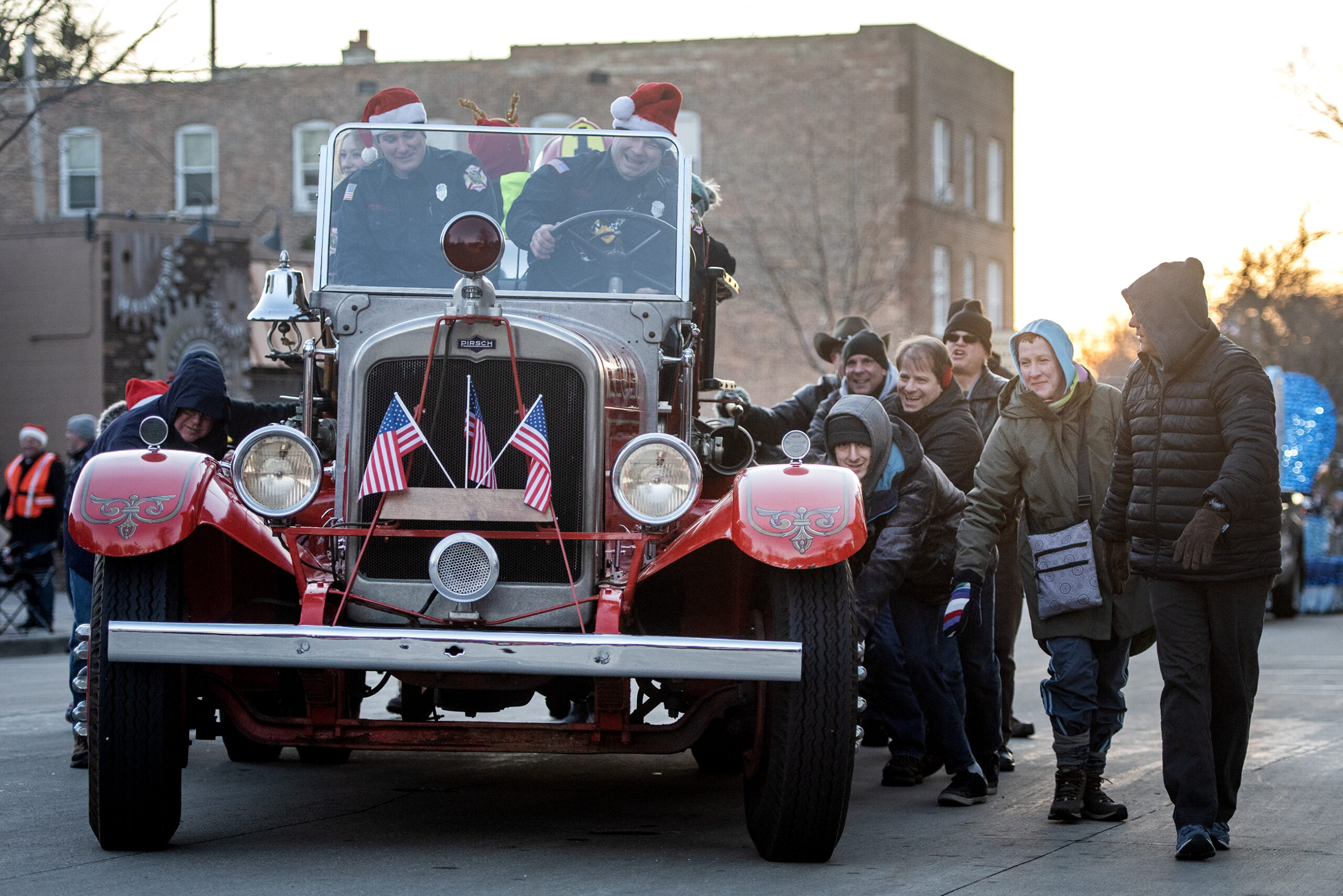 A group of people help to push a vintage style truck in the parade.