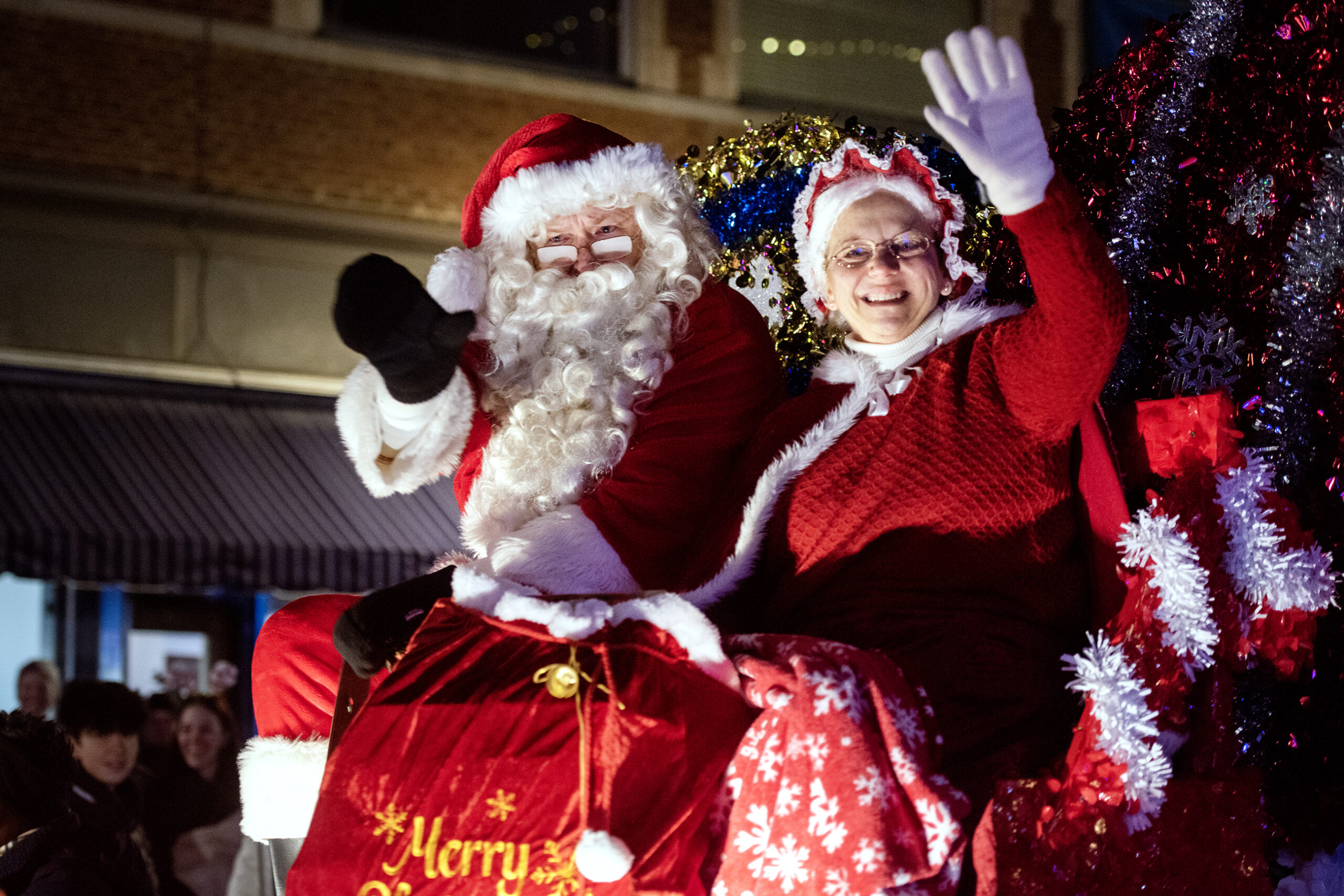 Sanda Claus and Mrs. Claus wave and smile at the crowd from a parade float.