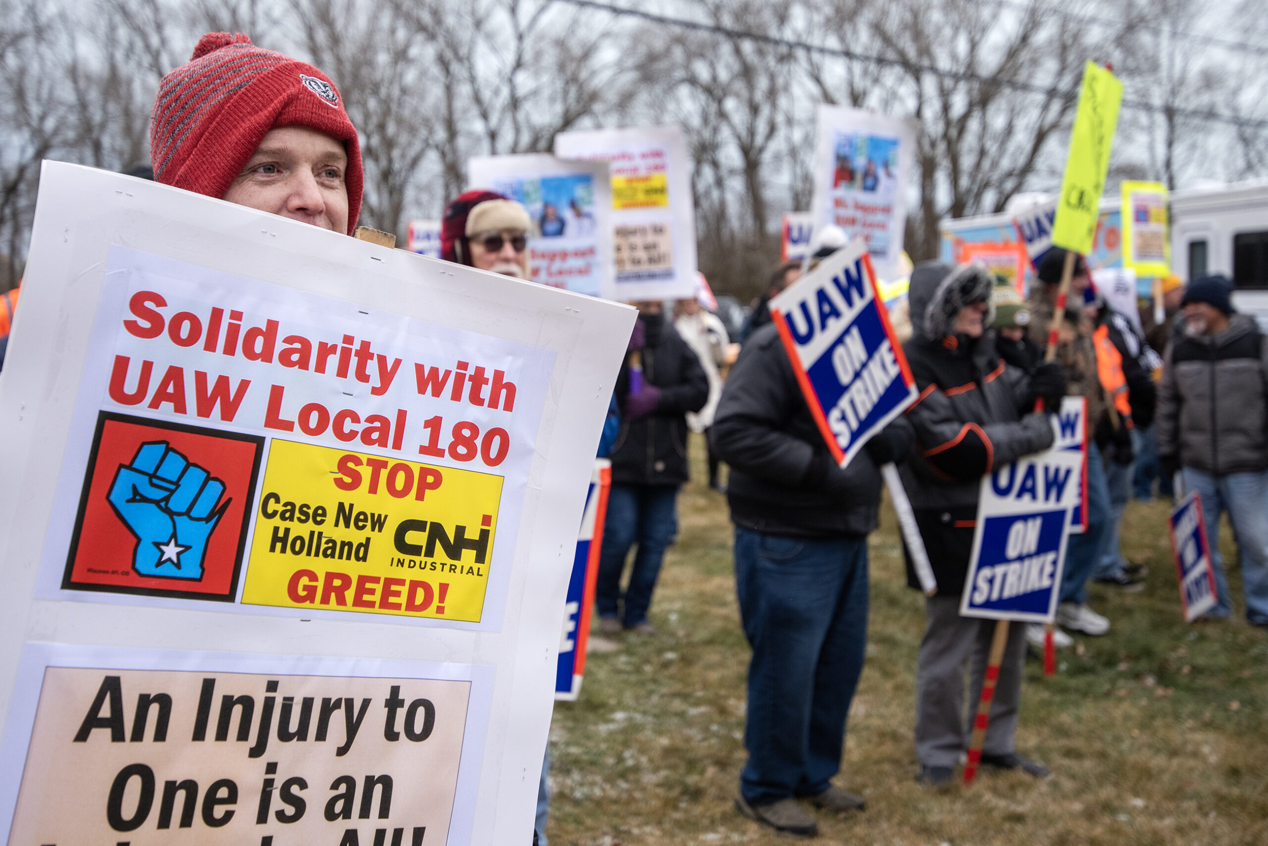 An attendee holds a sign that says "Solidarity with UAW Local 180" among other rally attendees.