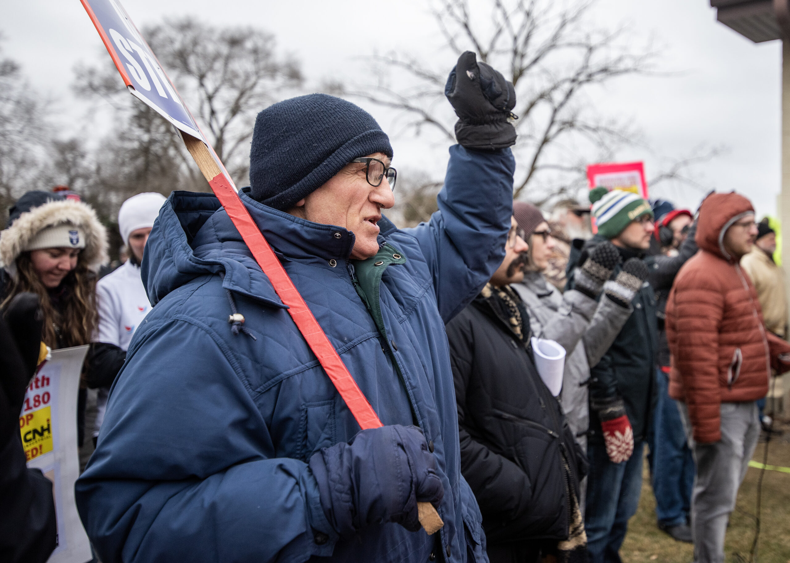 A man in a winter coat raises his fist as he holds a sign.