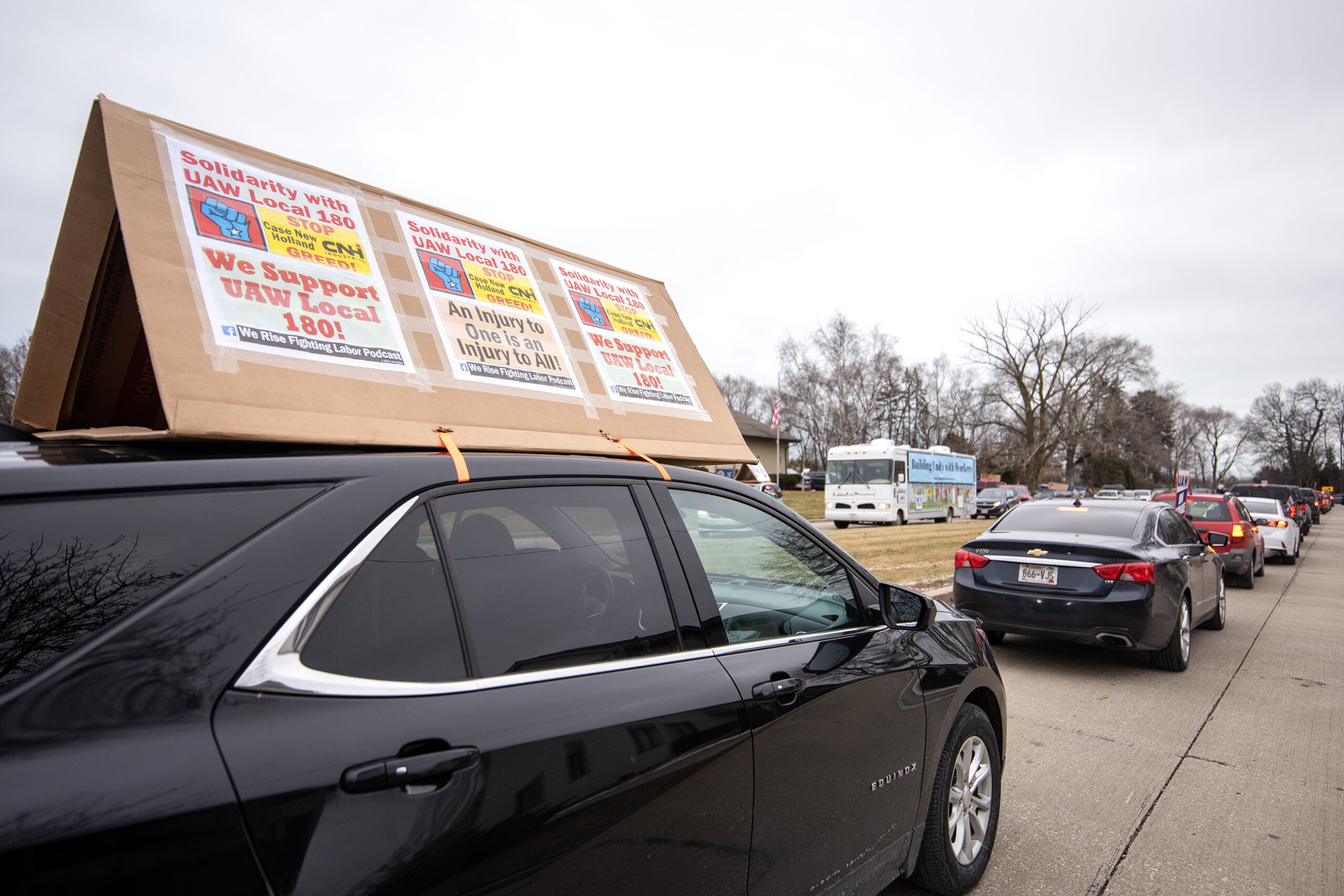 A cardboard sign is affixed to the top of a black car. Three signs in support of the union efforts are attached.