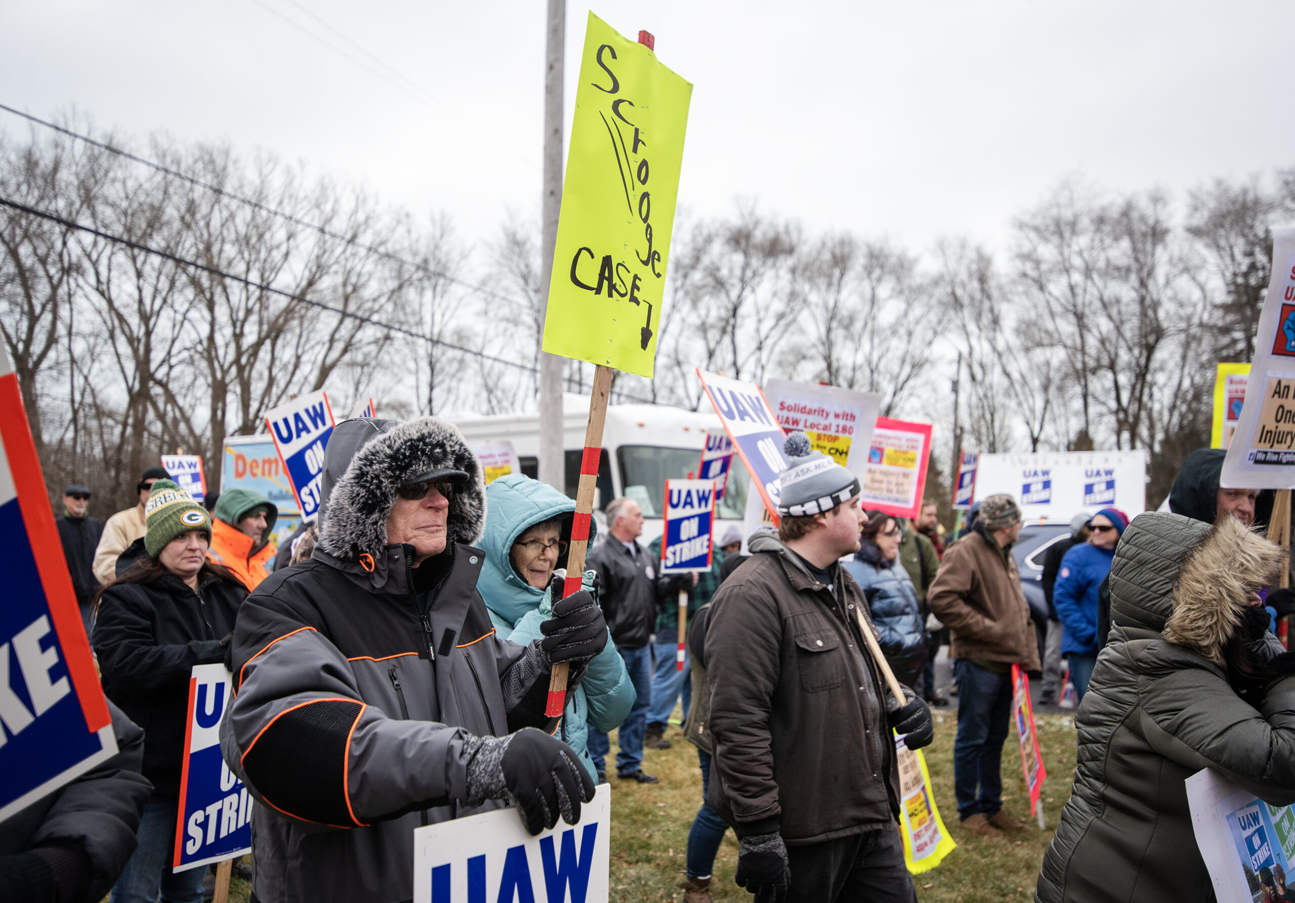 An attendee in a winter coat holds a sign that says 