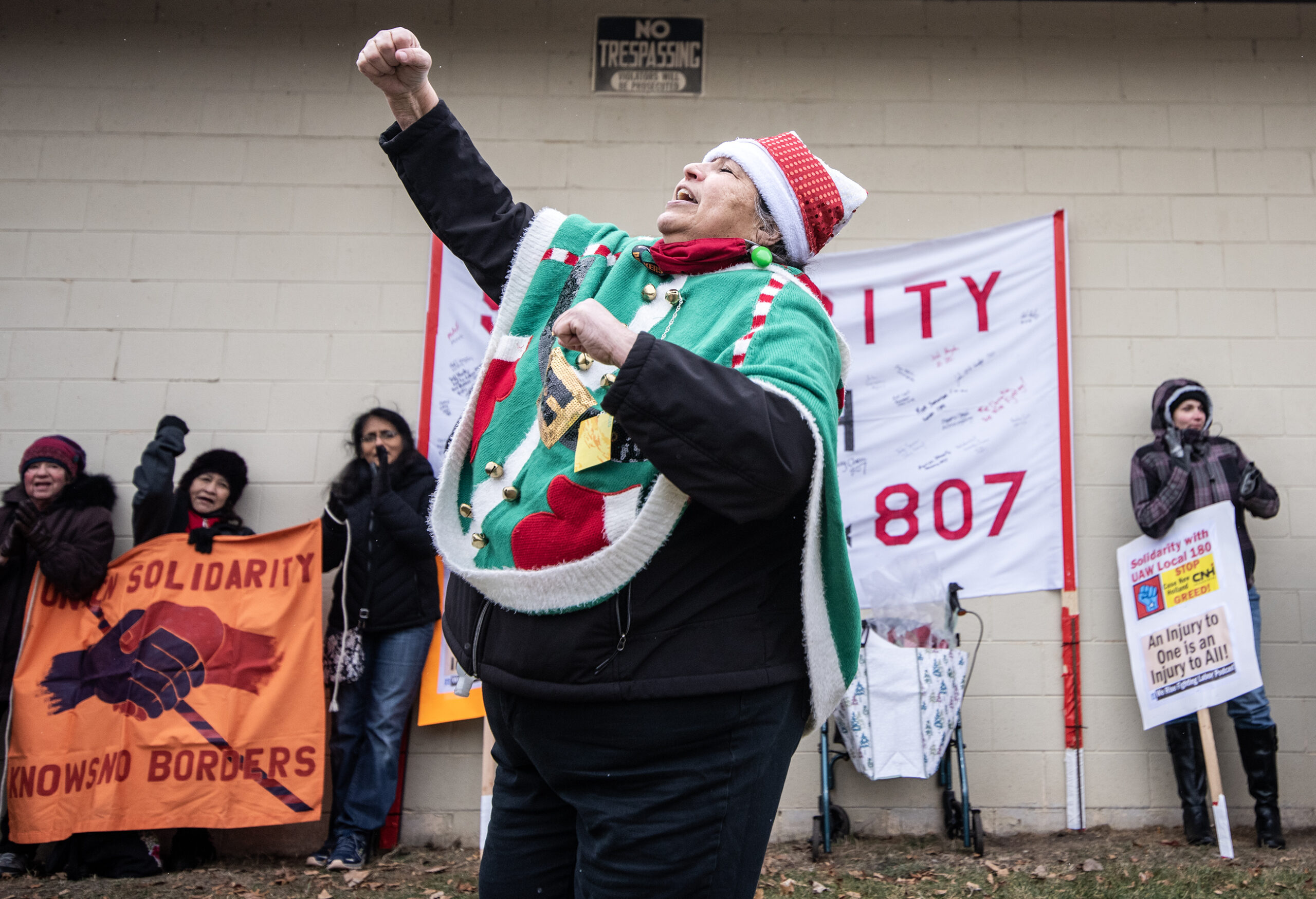 A woman in a Christmas themed outfit raises her fist while speaking to the rally.